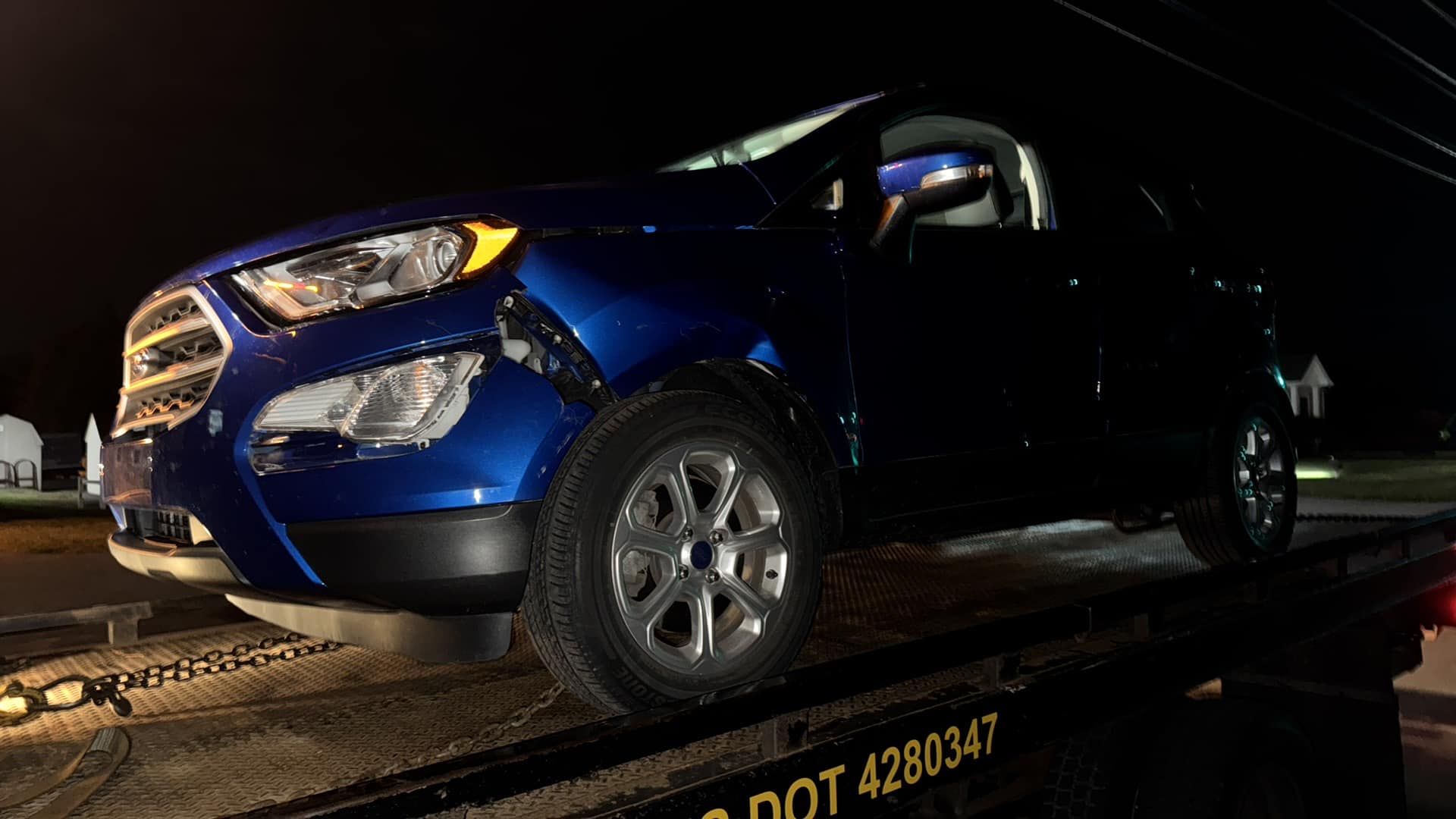 Blue SUV on a tow truck, damaged front end, night setting.