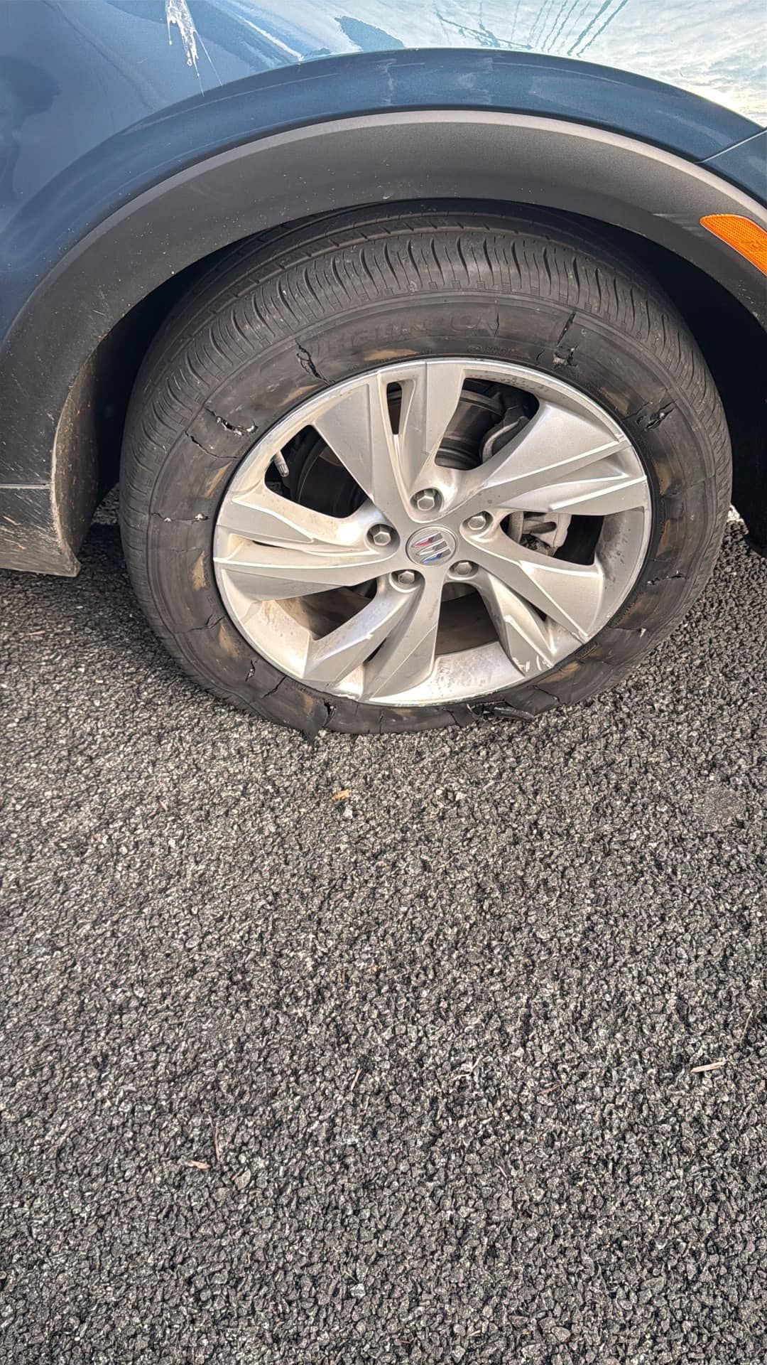 Close-up of a car's front tire on an asphalt surface. The tire is worn, and the wheel is silver.