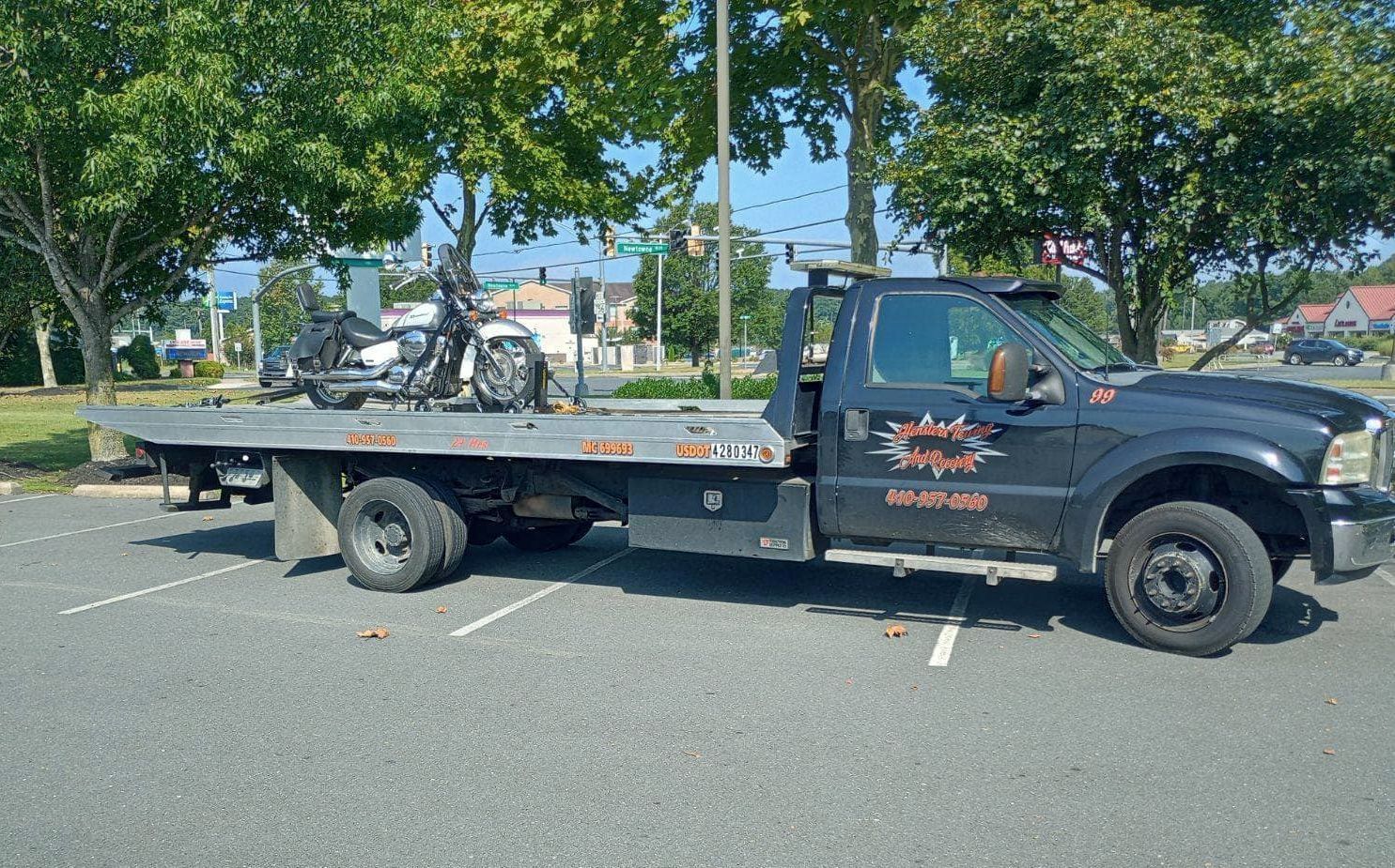 Black tow truck parked on asphalt. The truck bed holds a vehicle.