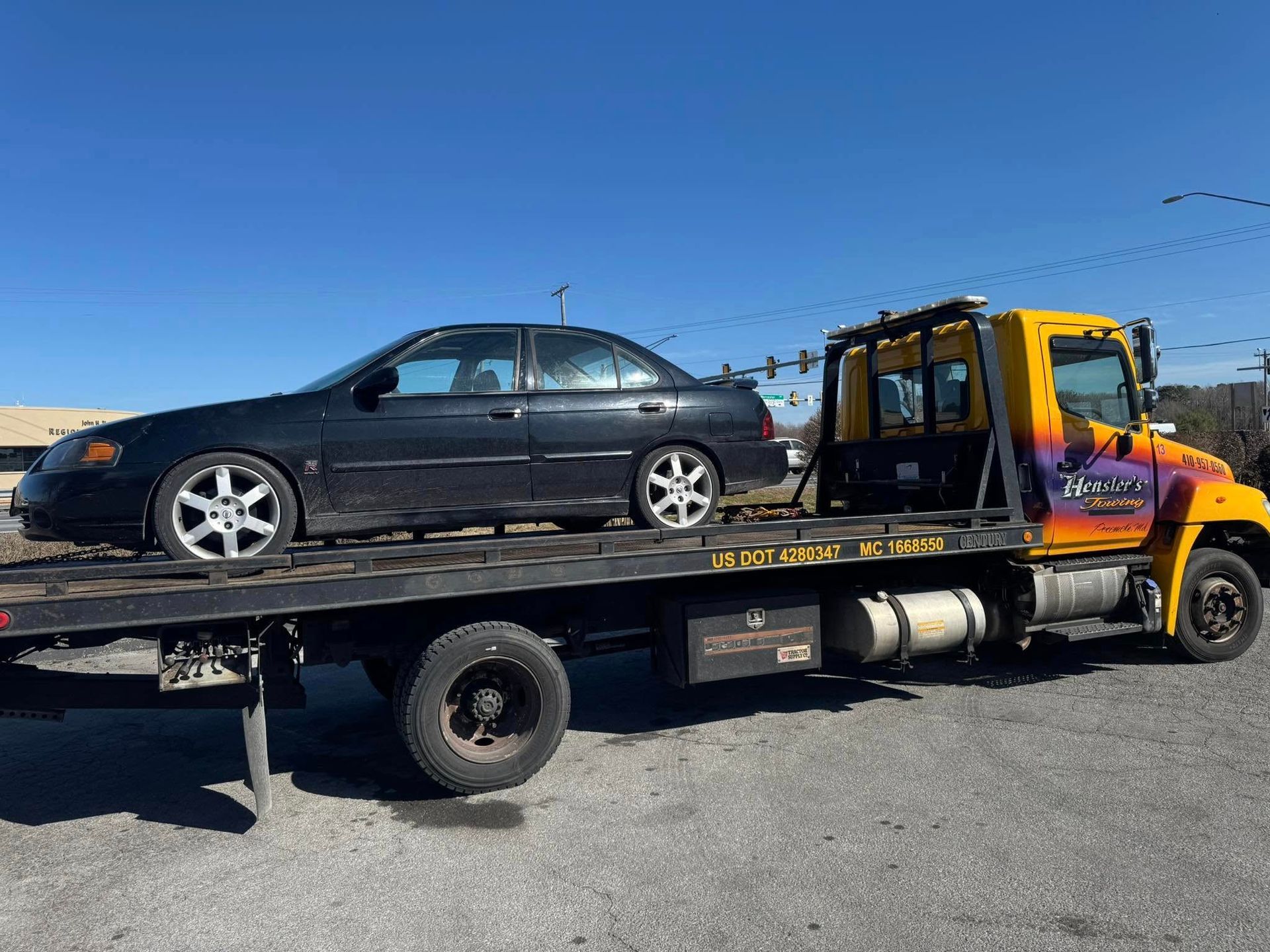 Black car being towed on a flatbed tow truck on a sunny day.