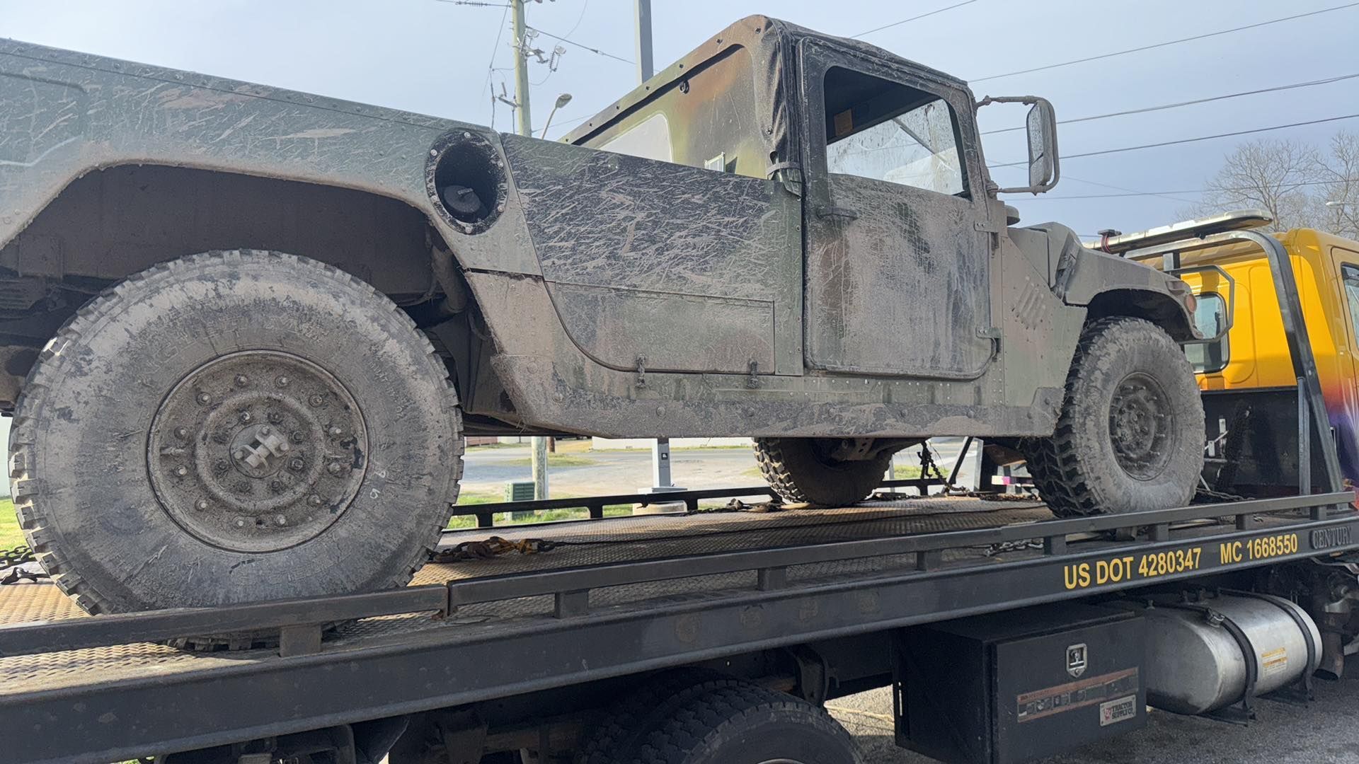 A military Humvee loaded on a tow truck, covered in mud and soot, roadside.