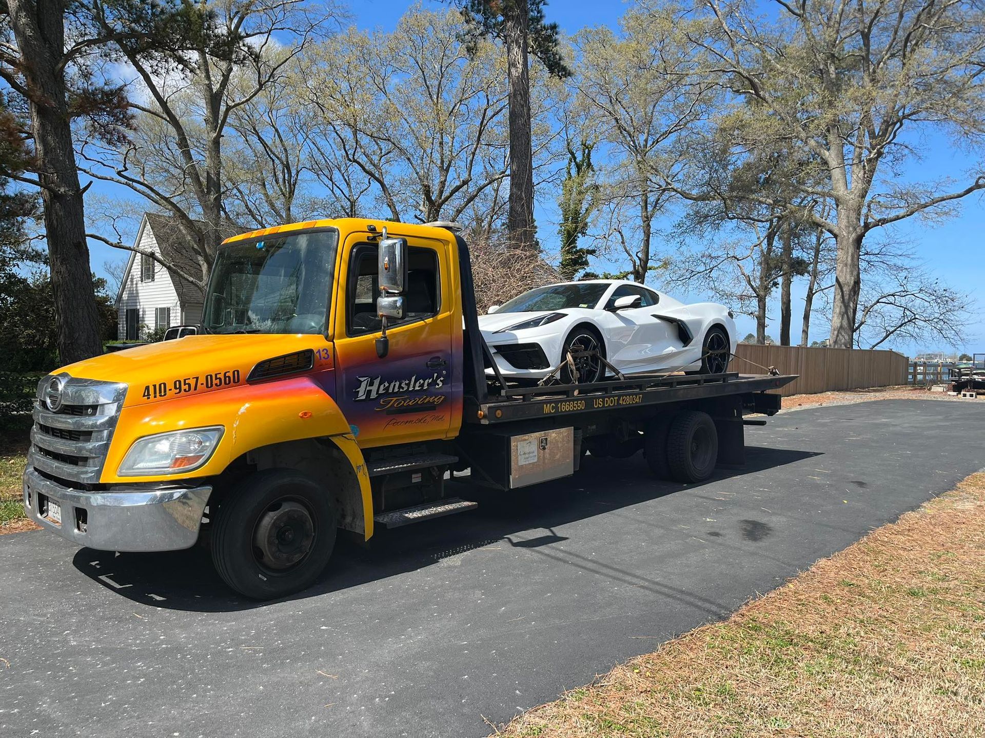 Yellow tow truck with a white sports car on its bed, parked on a road.
