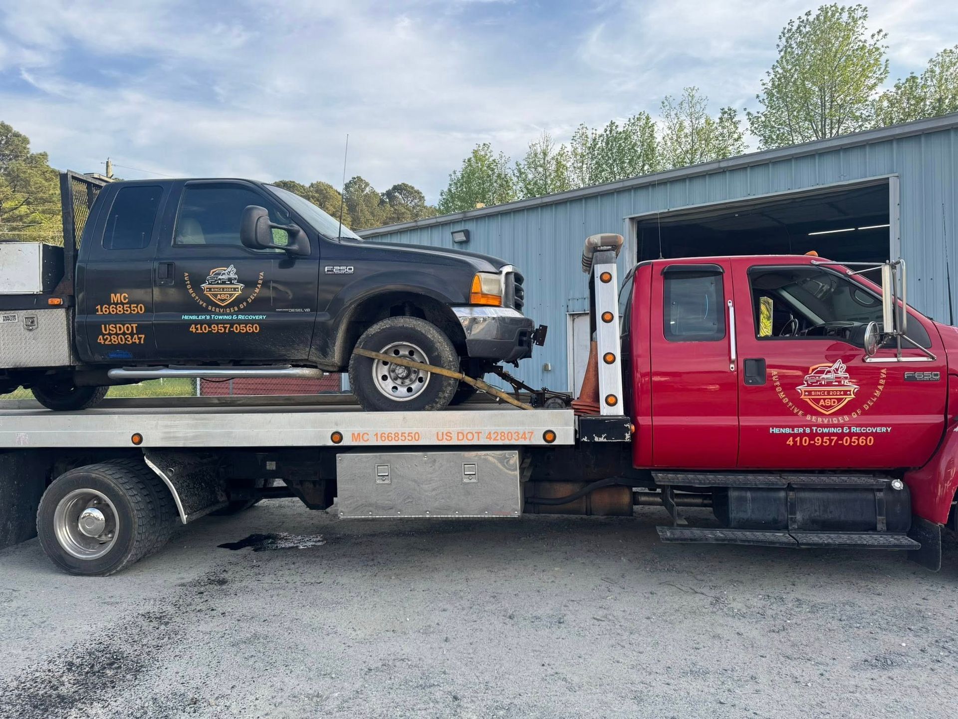 A black pickup truck being towed by a red tow truck, outdoors in front of a building.