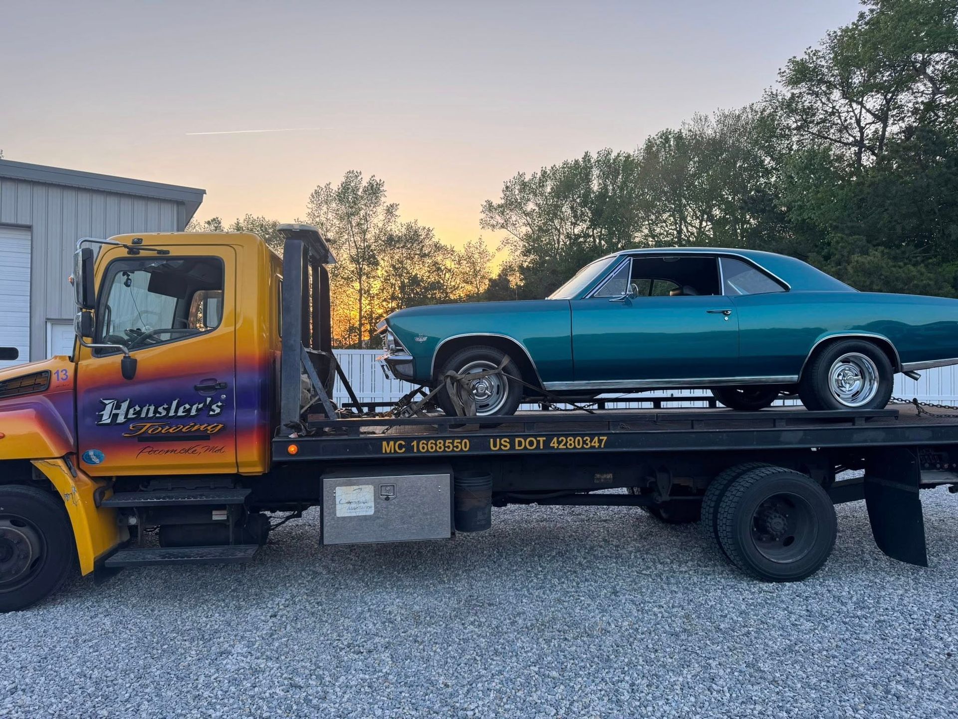 Teal classic car on a flatbed tow truck at sunset.