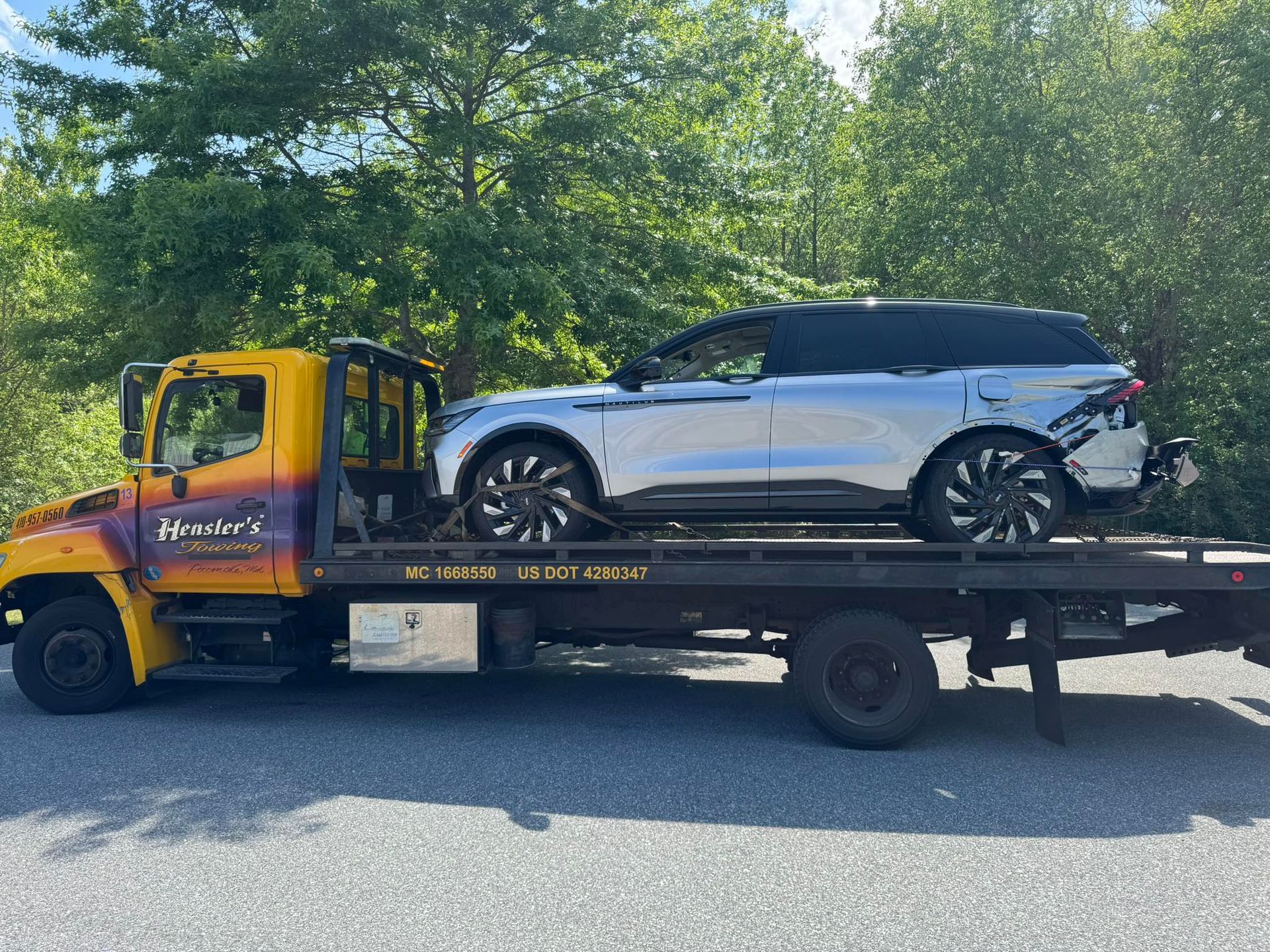 Tow truck with a silver SUV on its flatbed, outdoors.
