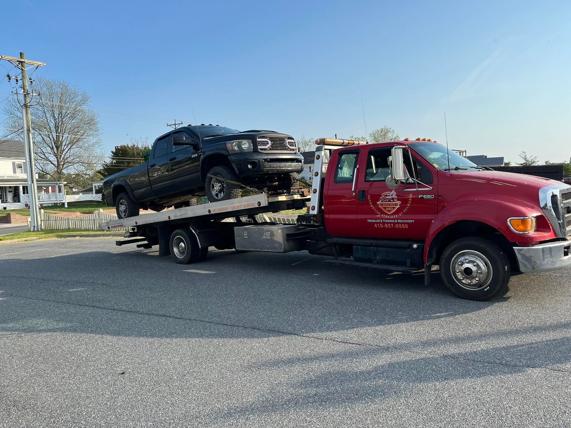 A red tow truck carrying a black pickup truck on a flatbed, parked outdoors.