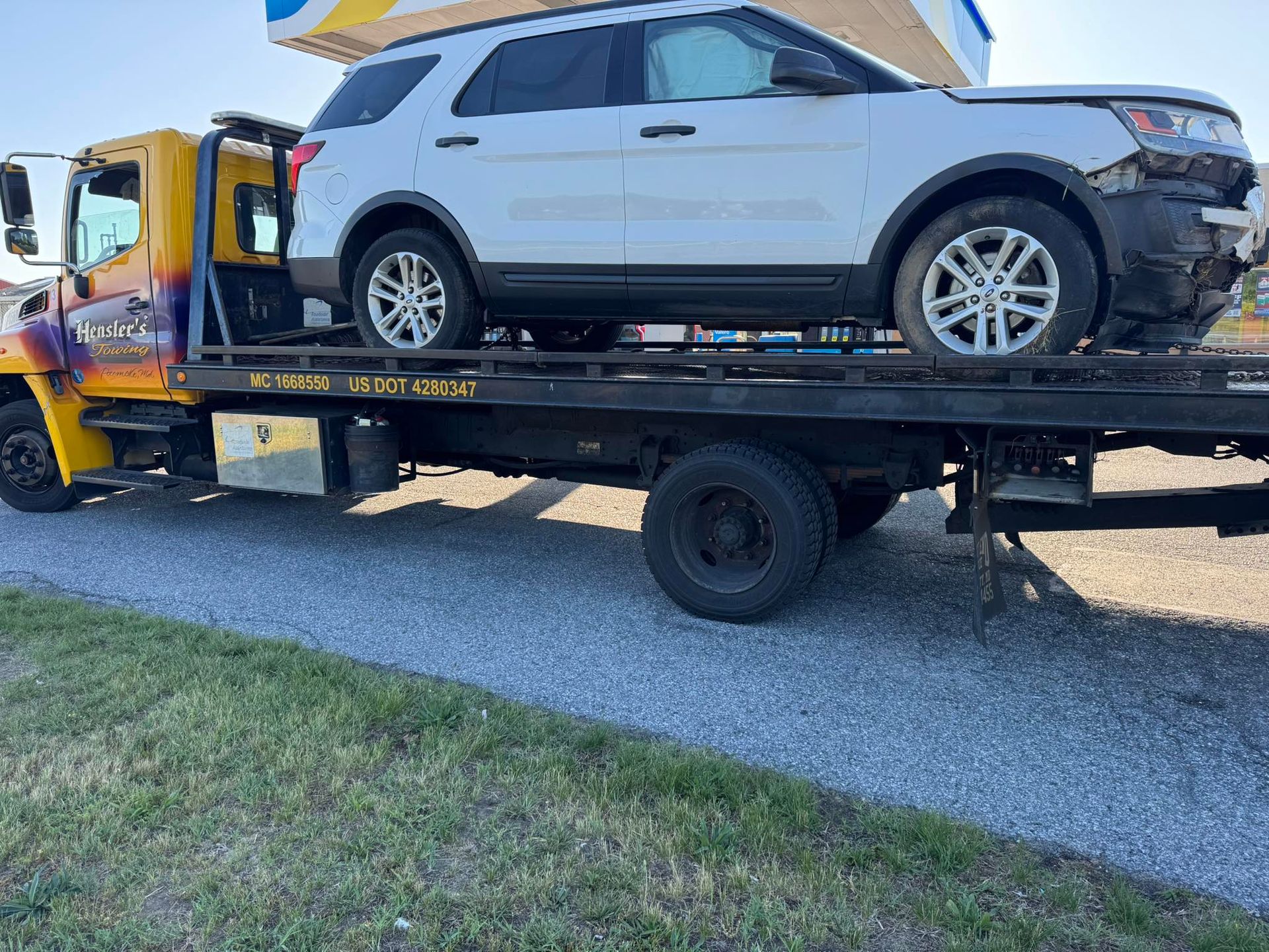 White SUV on a flatbed tow truck with front-end damage; parked on asphalt.