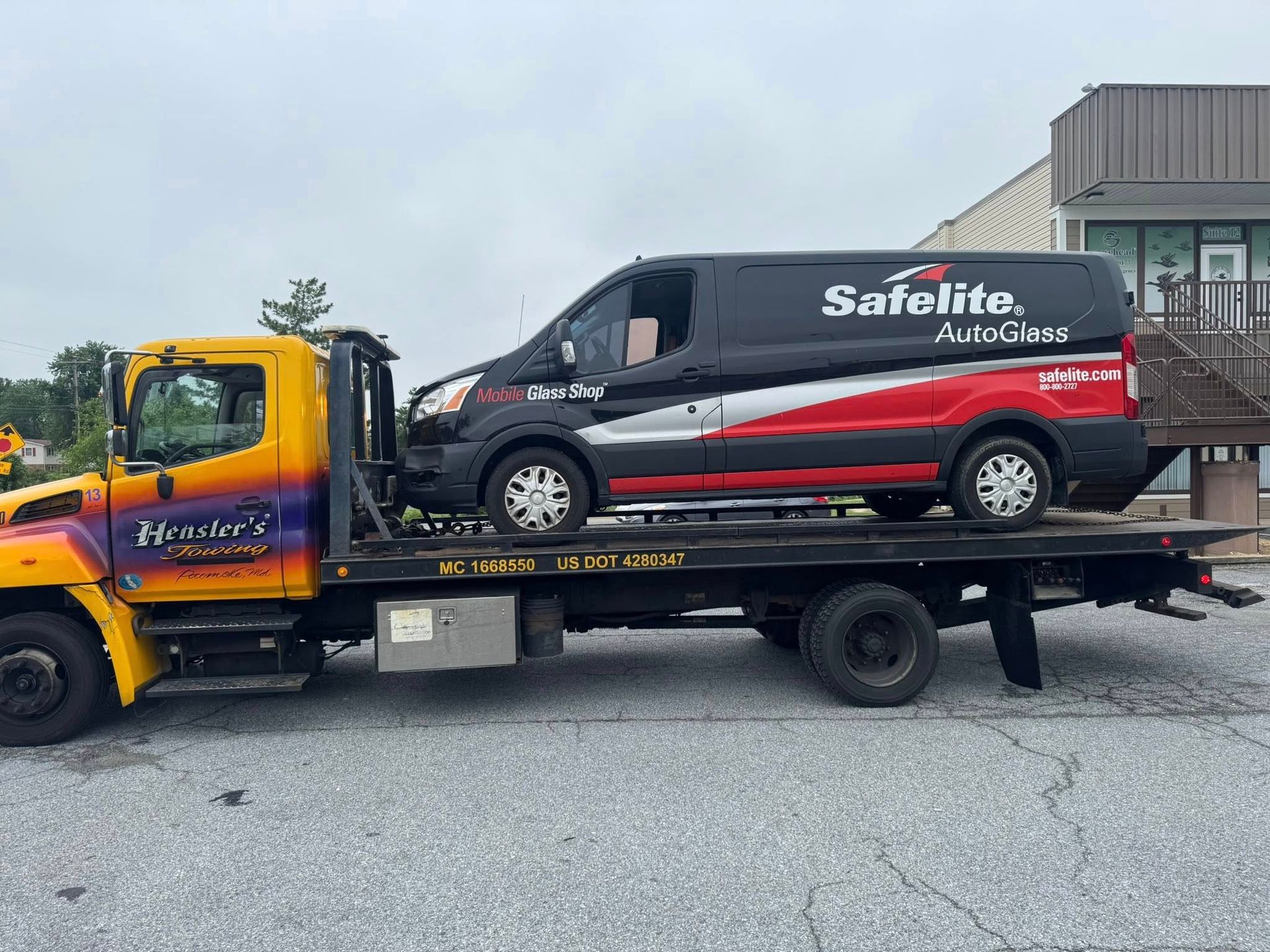 Tow truck with a black and red Safelite AutoGlass van on its flatbed.