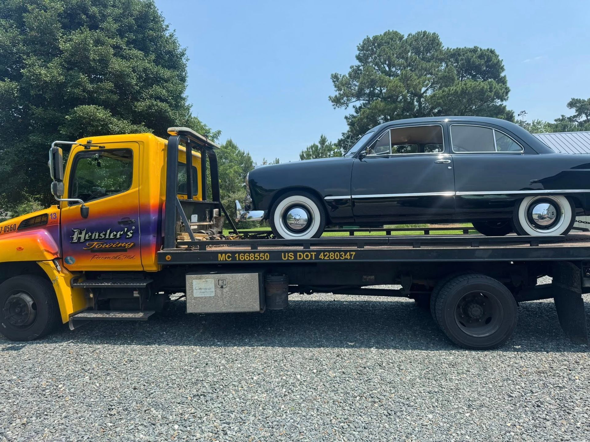 Black classic car on a yellow tow truck on a sunny day.