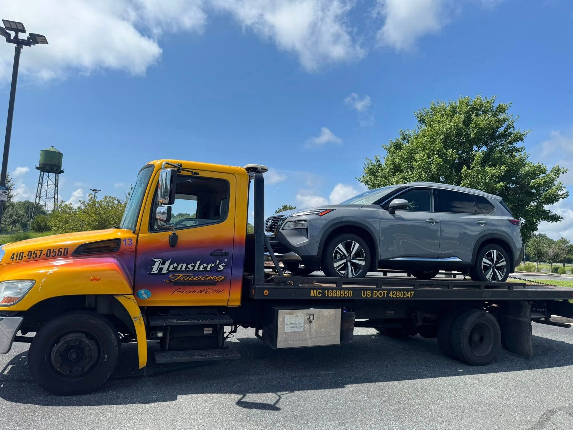 Yellow tow truck with a gray SUV on its bed, under a partly cloudy sky.
