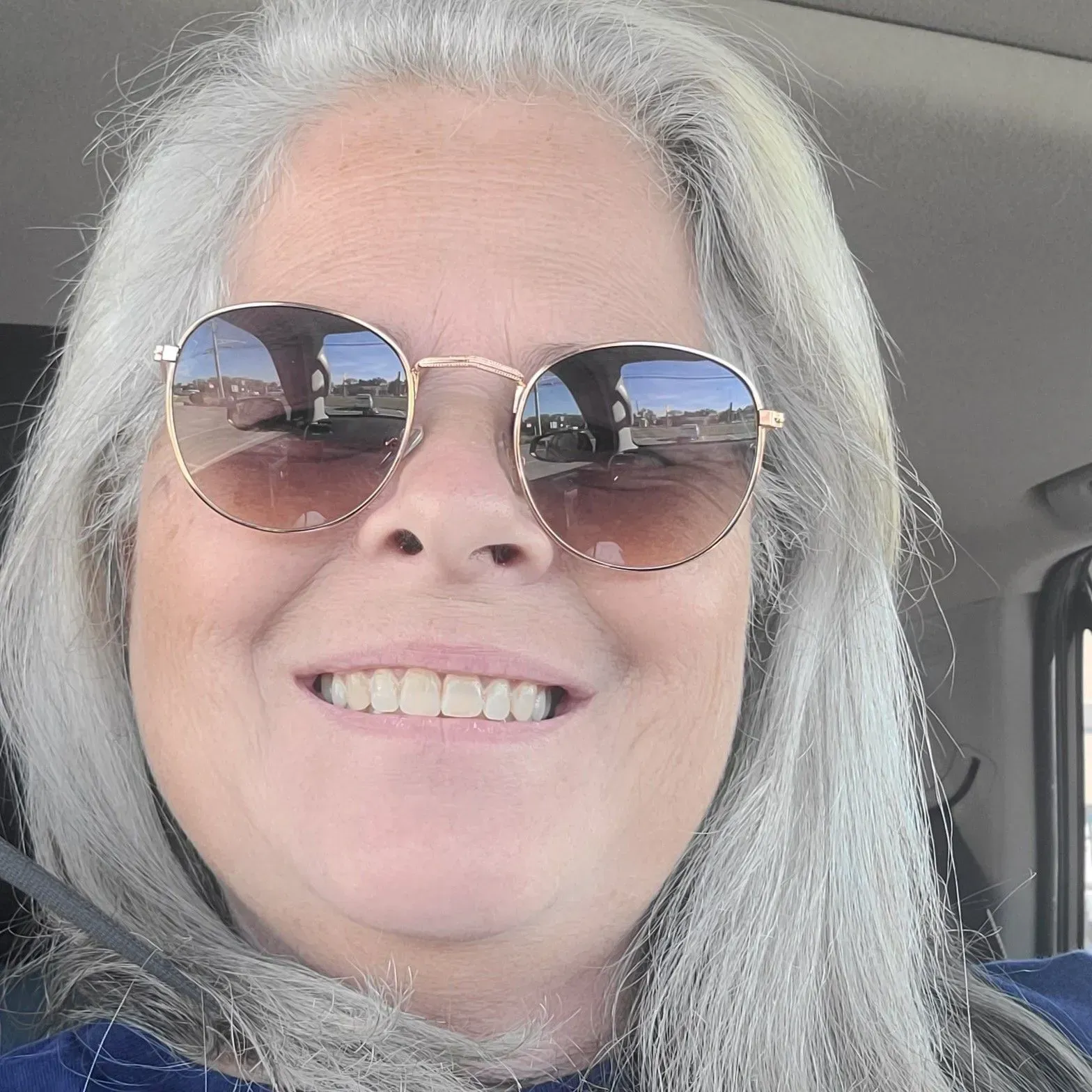 Woman with gray hair and sunglasses smiling in a car.