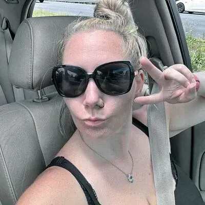 Woman in sunglasses making peace sign, sitting in a car.