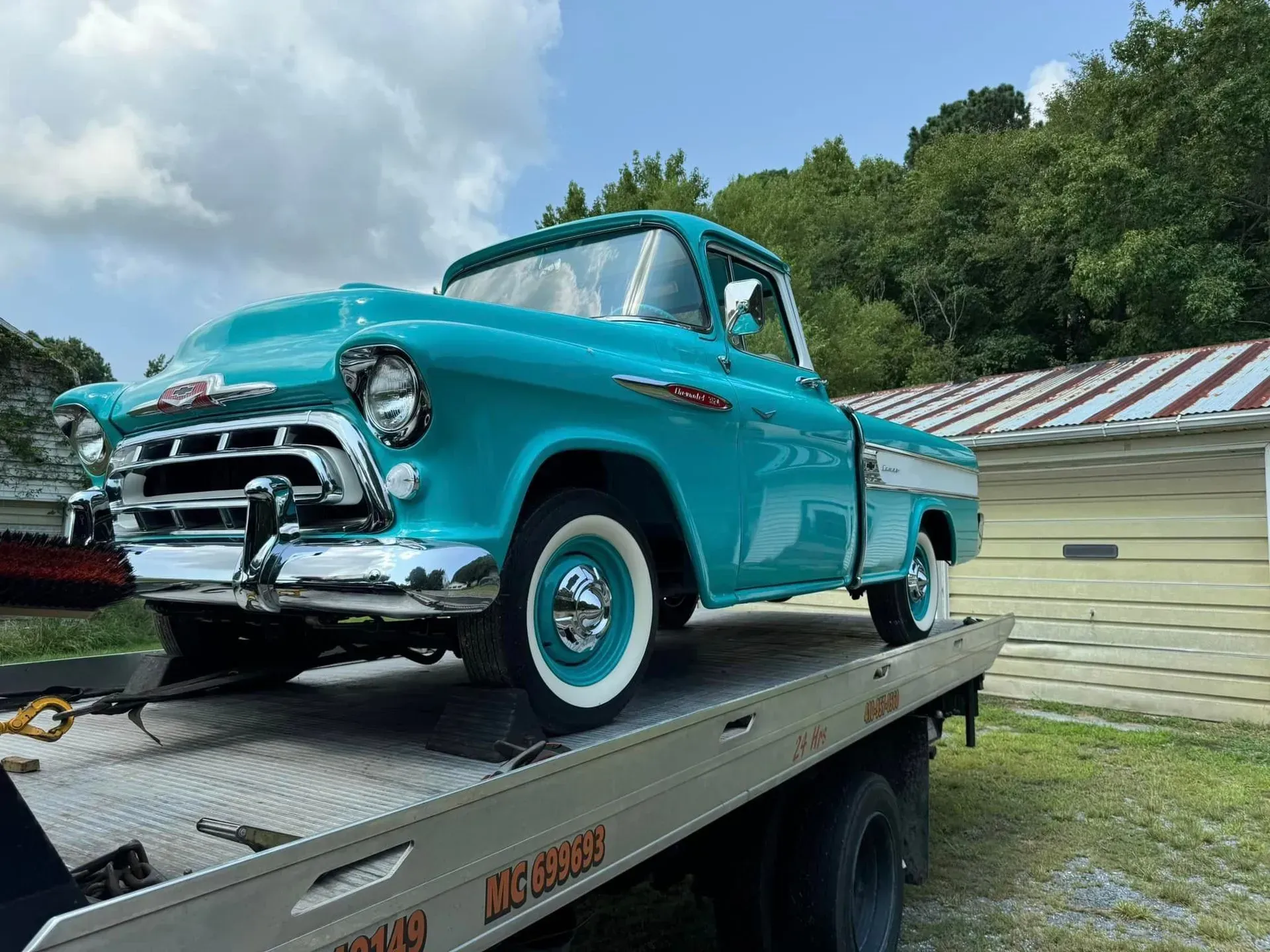 Teal vintage Chevrolet pickup truck on a tow truck in front of a building.
