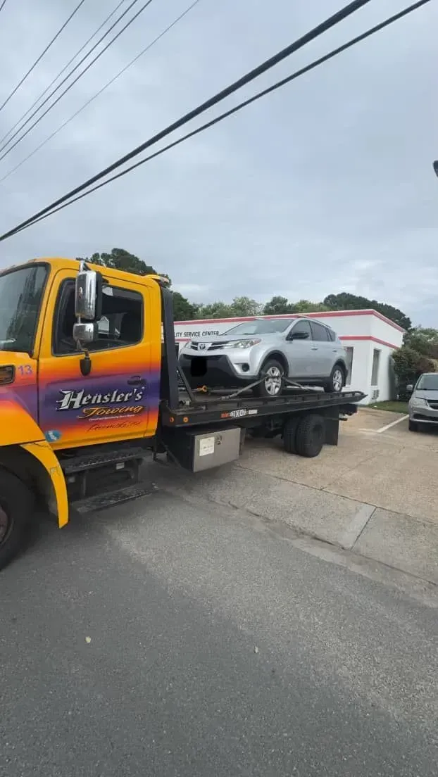 A silver car is on a flatbed tow truck with the name 