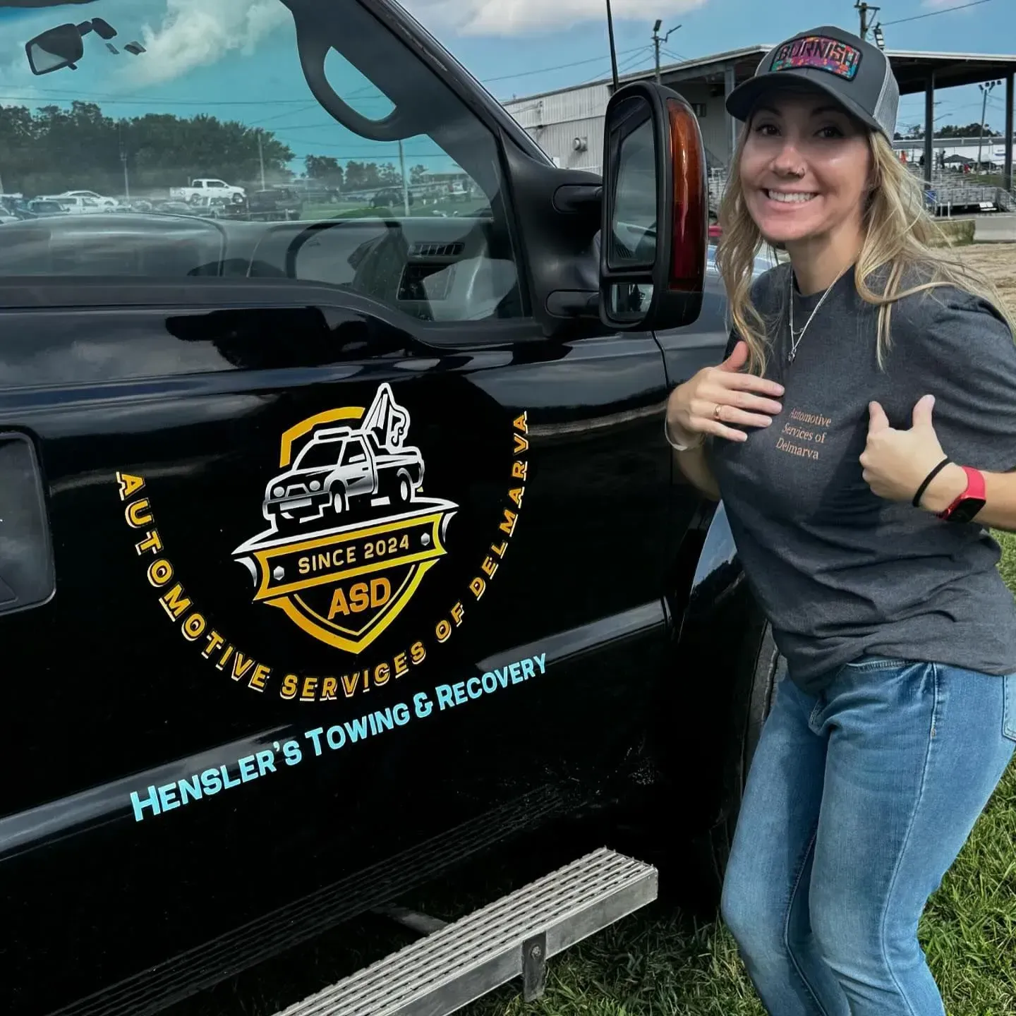 Woman stands next to black tow truck, smiling. The truck has a company logo on the door.