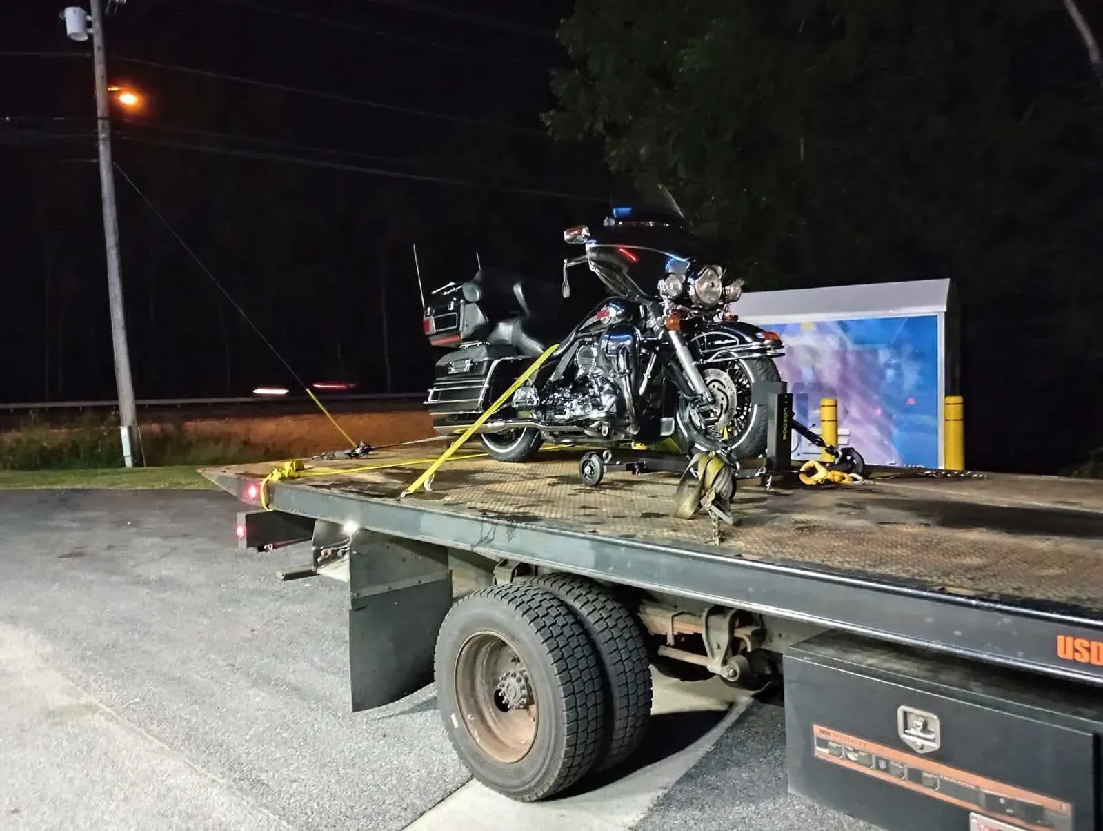 Motorcycle on a flatbed tow truck at night, secured with straps.