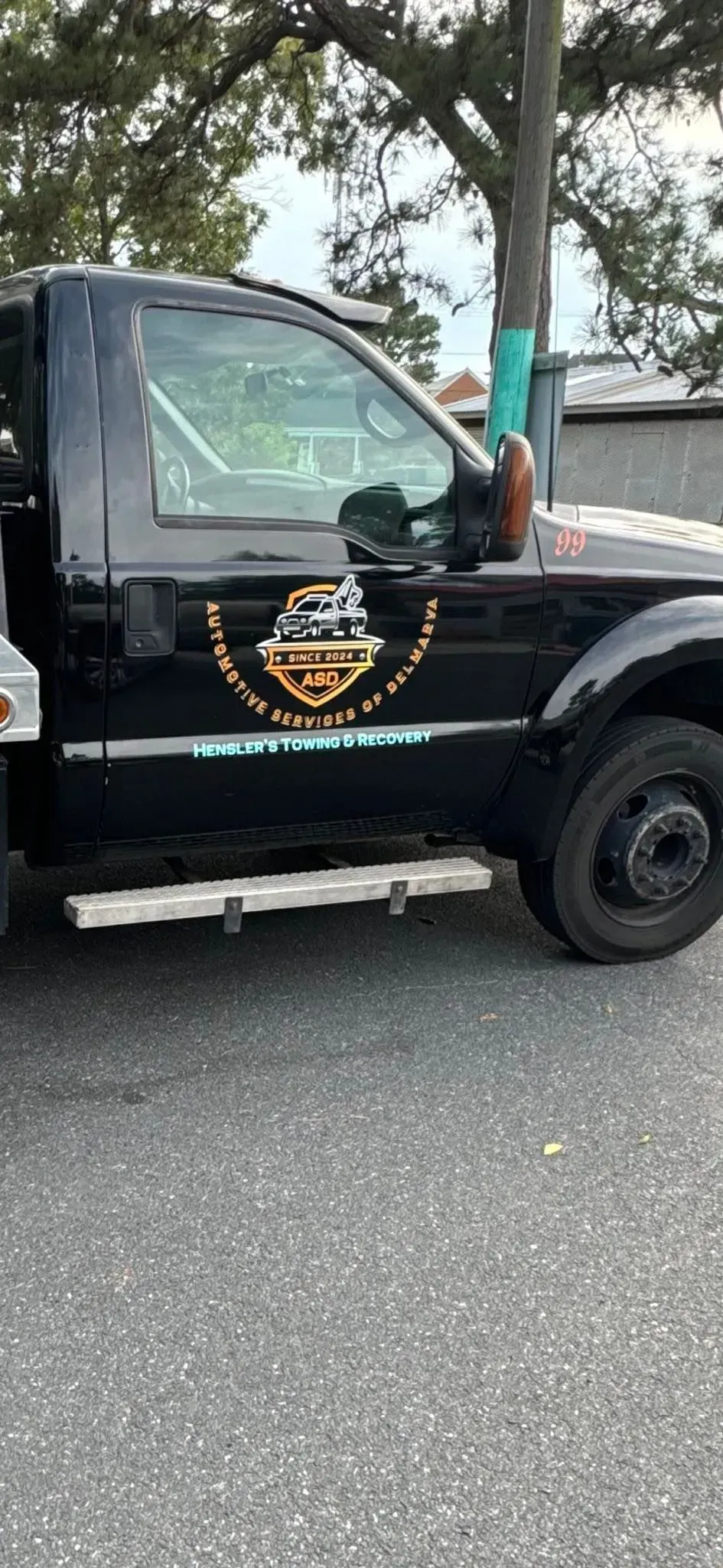 Black tow truck with logo on the door, parked on a paved road.