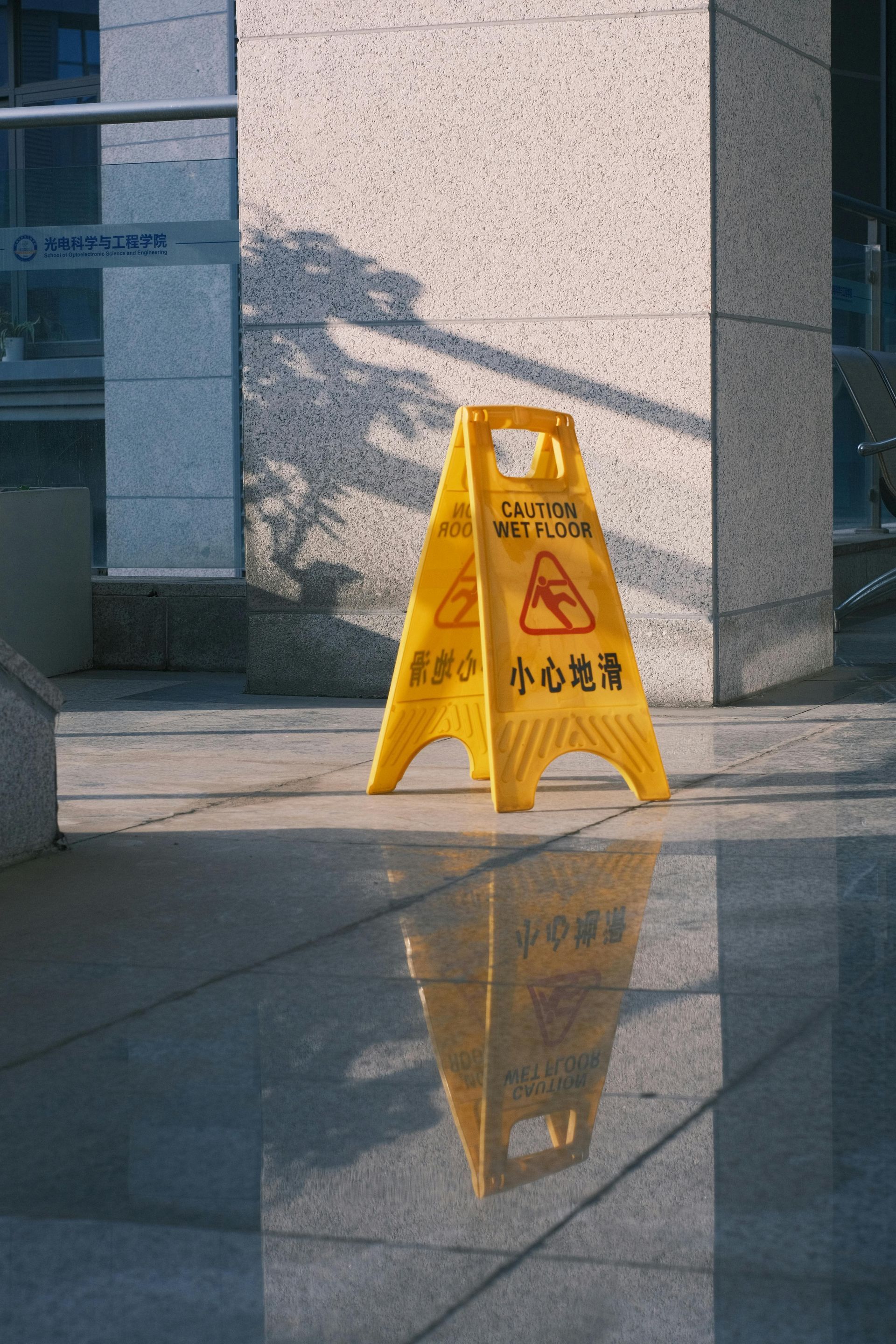 A yellow caution sign is sitting on the ground in front of a building.