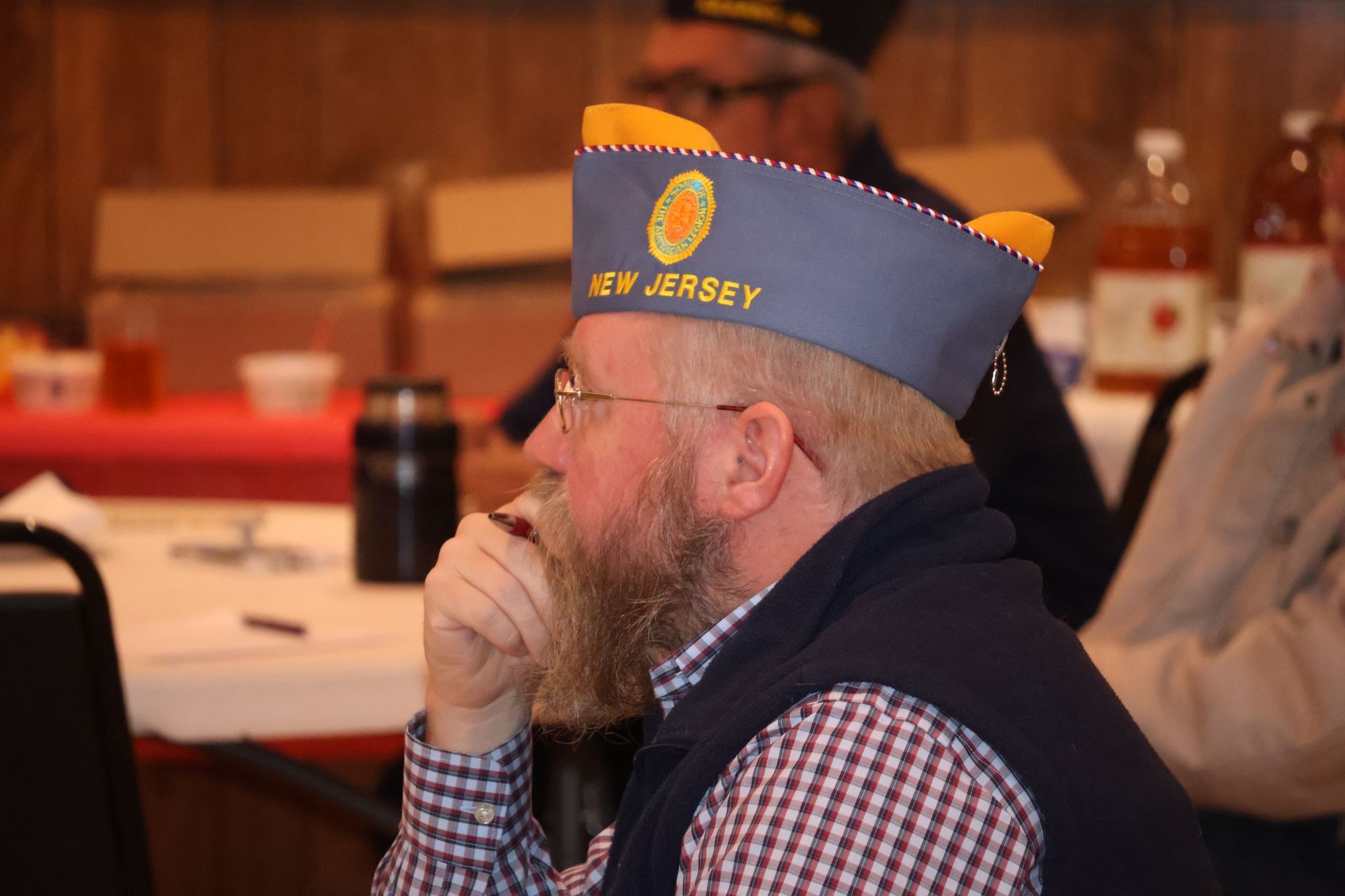 Man wearing a New Jersey veterans cap, seated at a table, looking to the side.