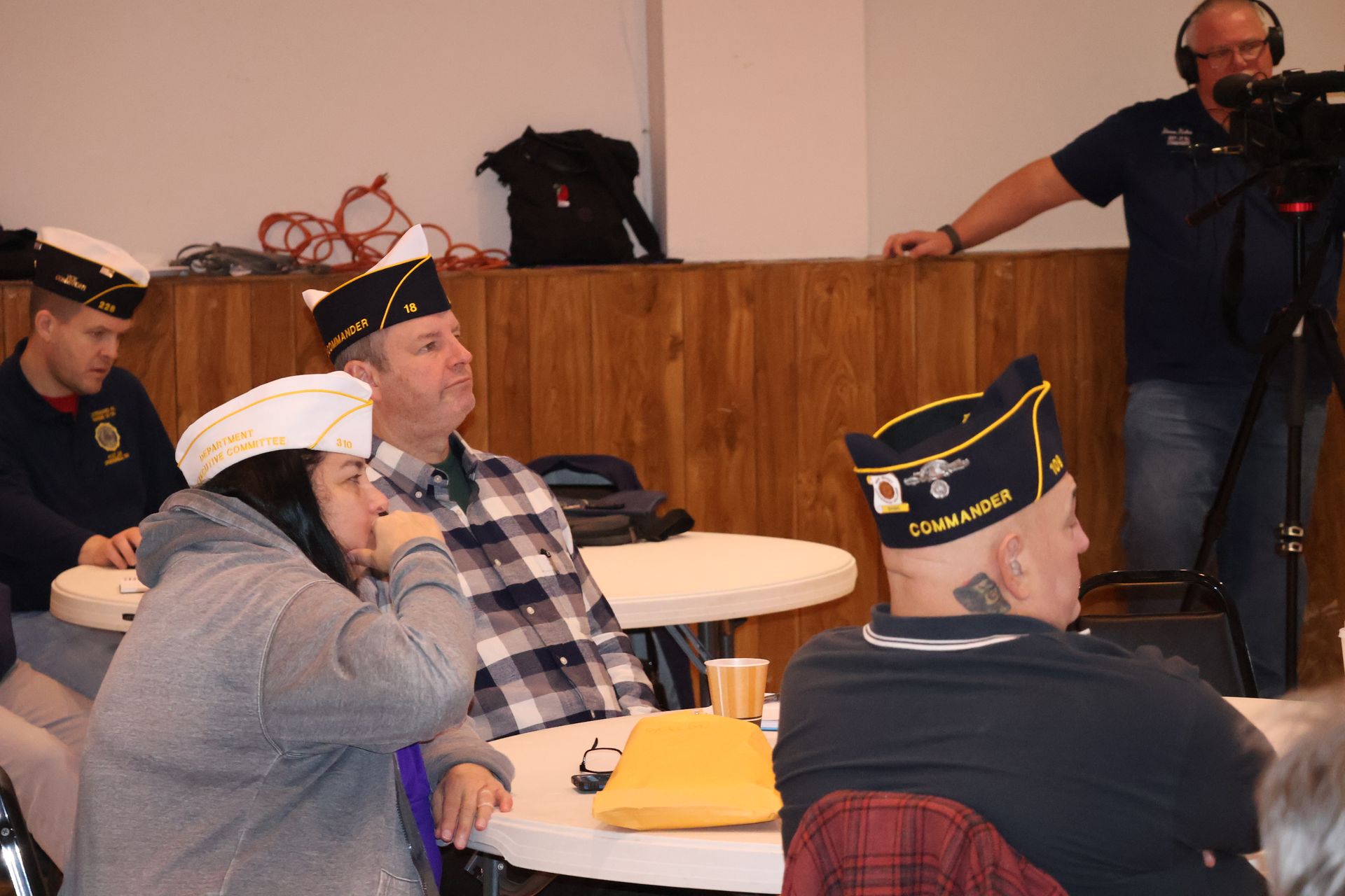 Group of people in hats at tables, being filmed.