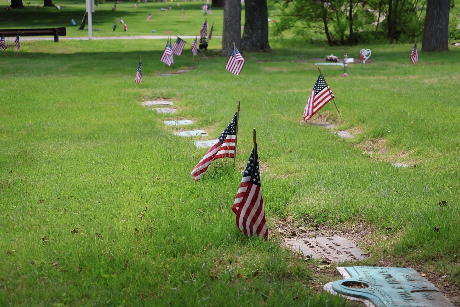 Small American flags marking graves in a green cemetery lawn