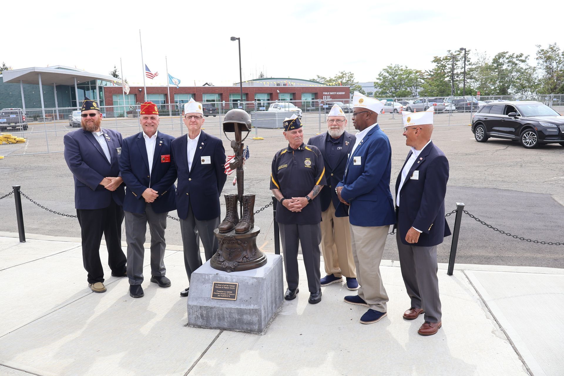 Group of veterans standing near a bronze war memorial statue outdoors.