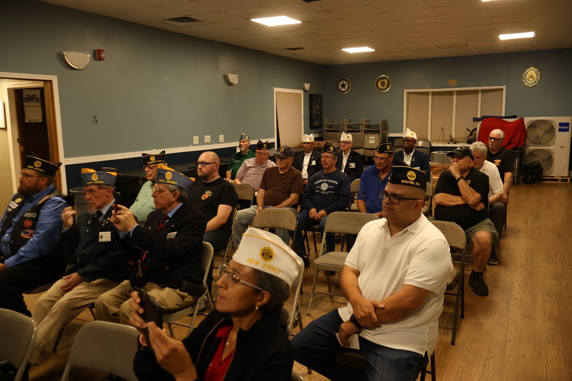 Group of people seated in a room, some wearing hats, listening to a presentation.
