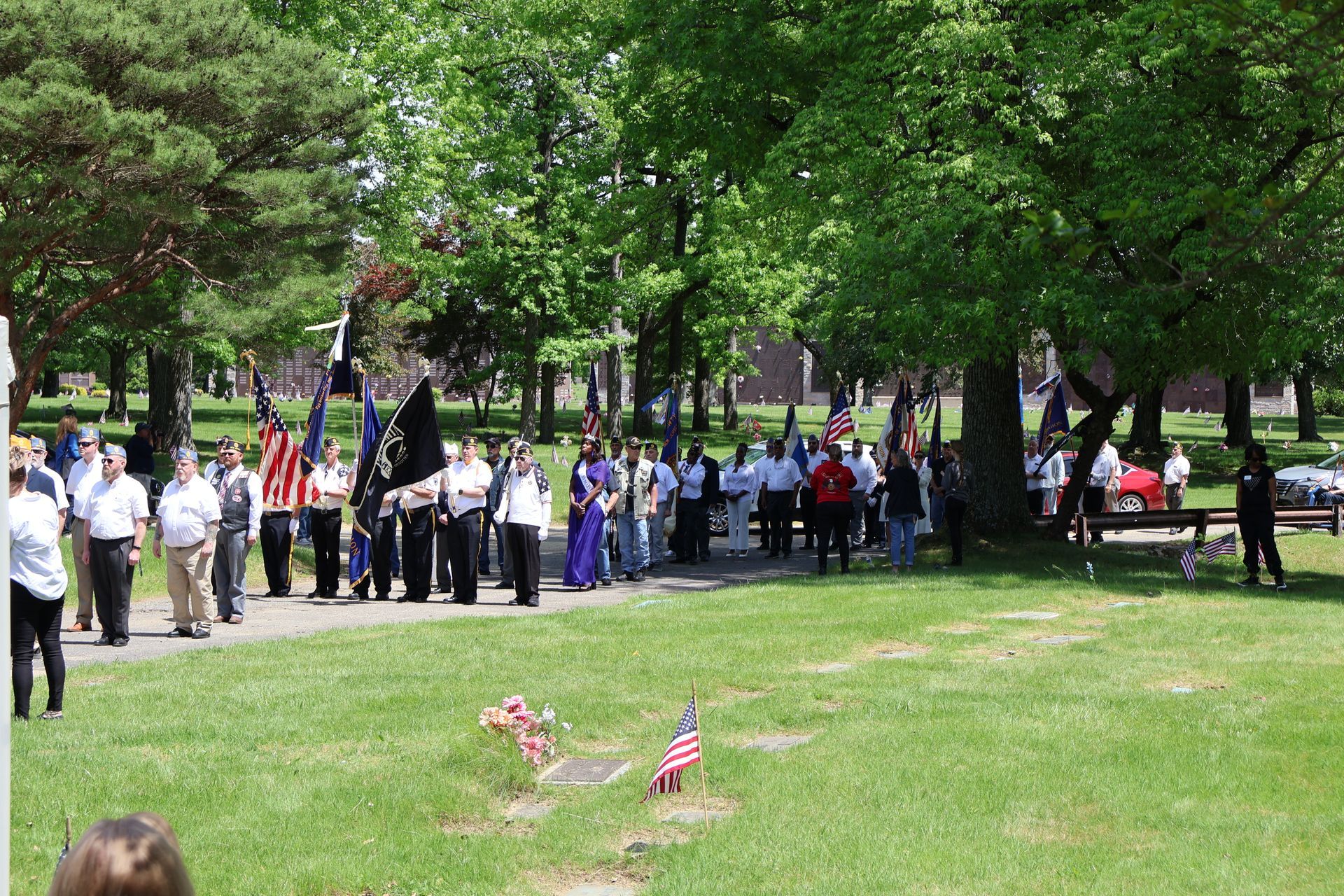 People gathered in a park for a memorial, with small American flags on a grassy lawn.