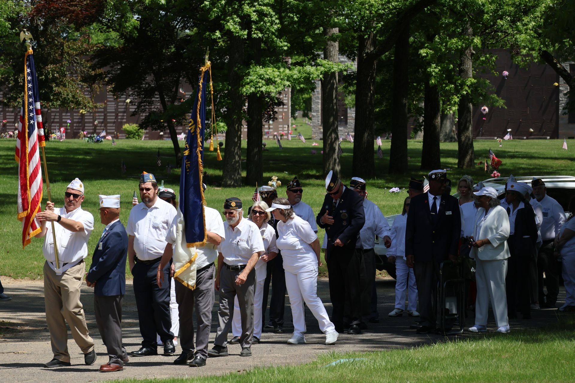 People gathered in a park holding American flags during a small outdoor ceremony.
