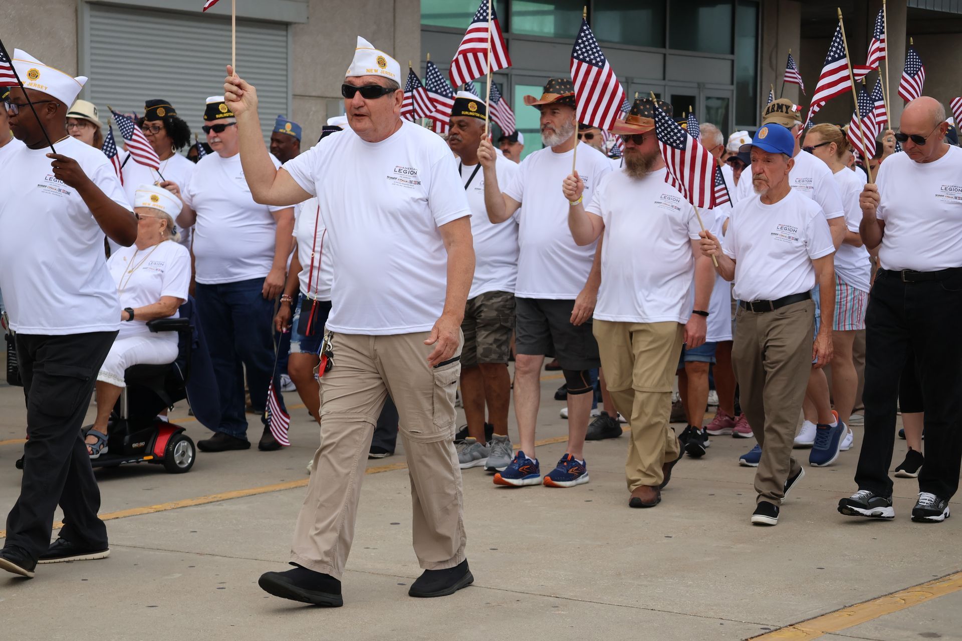 Group of people in white shirts and hats marching, holding American flags.