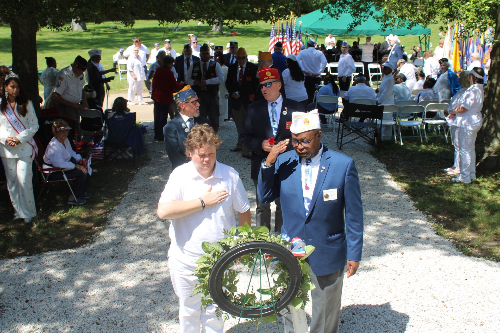 People standing at an outdoor memorial wreath-laying ceremony with flags and folding chairs.