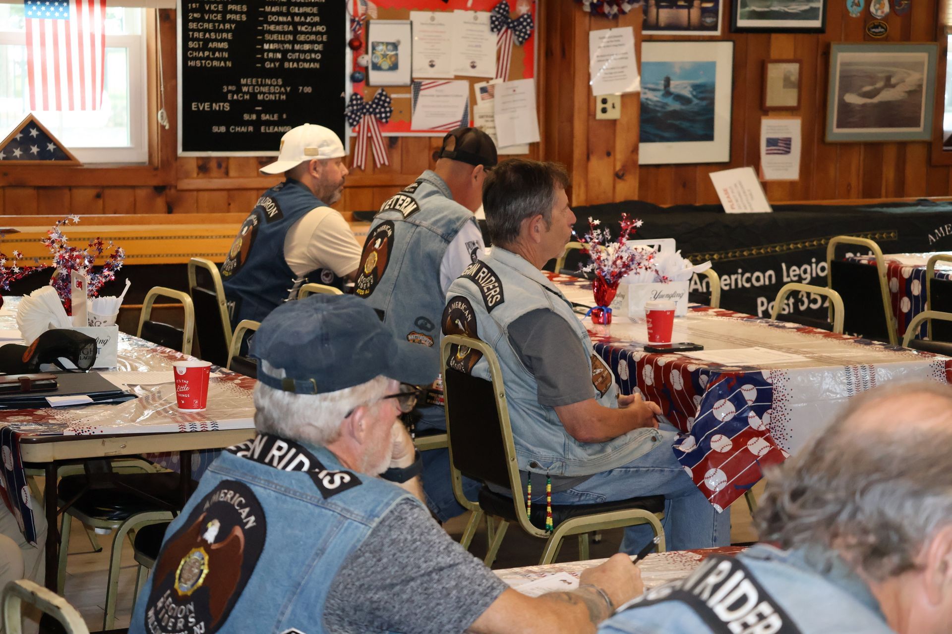 Men in denim vests at a decorated table, possibly a veteran's event, with patriotic decorations.