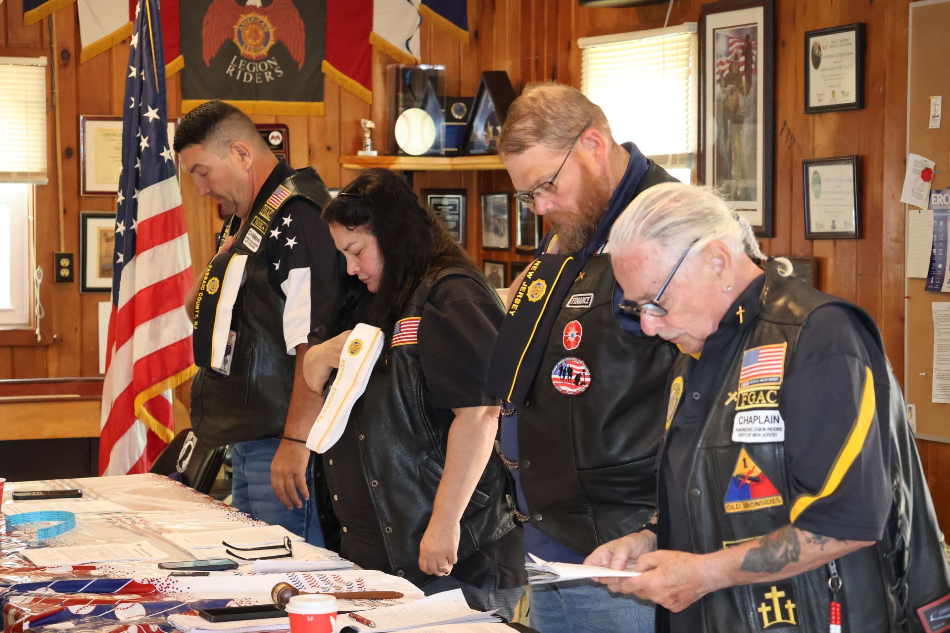 People in leather vests examining papers at a table in a room with flags and decorations.