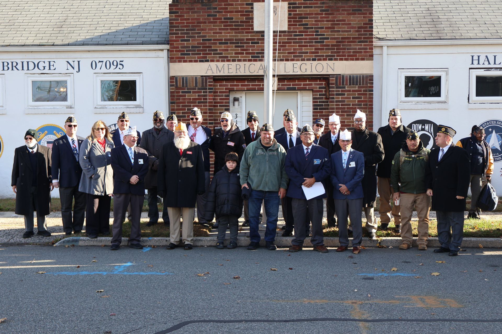 Group of people in front of an American Legion building. Many wear military hats.