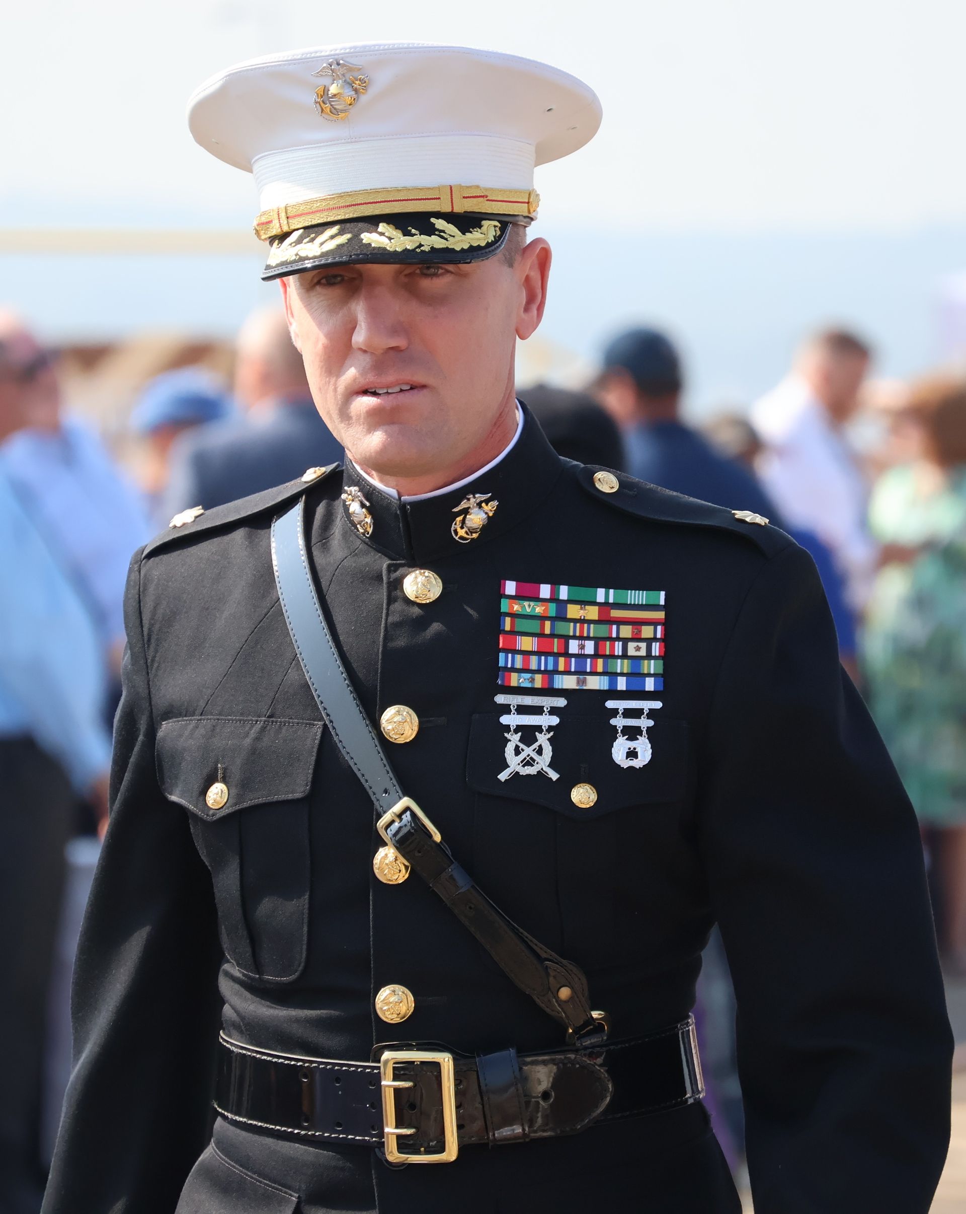 Marine officer in formal dress uniform, white hat, many service ribbons, looking down.