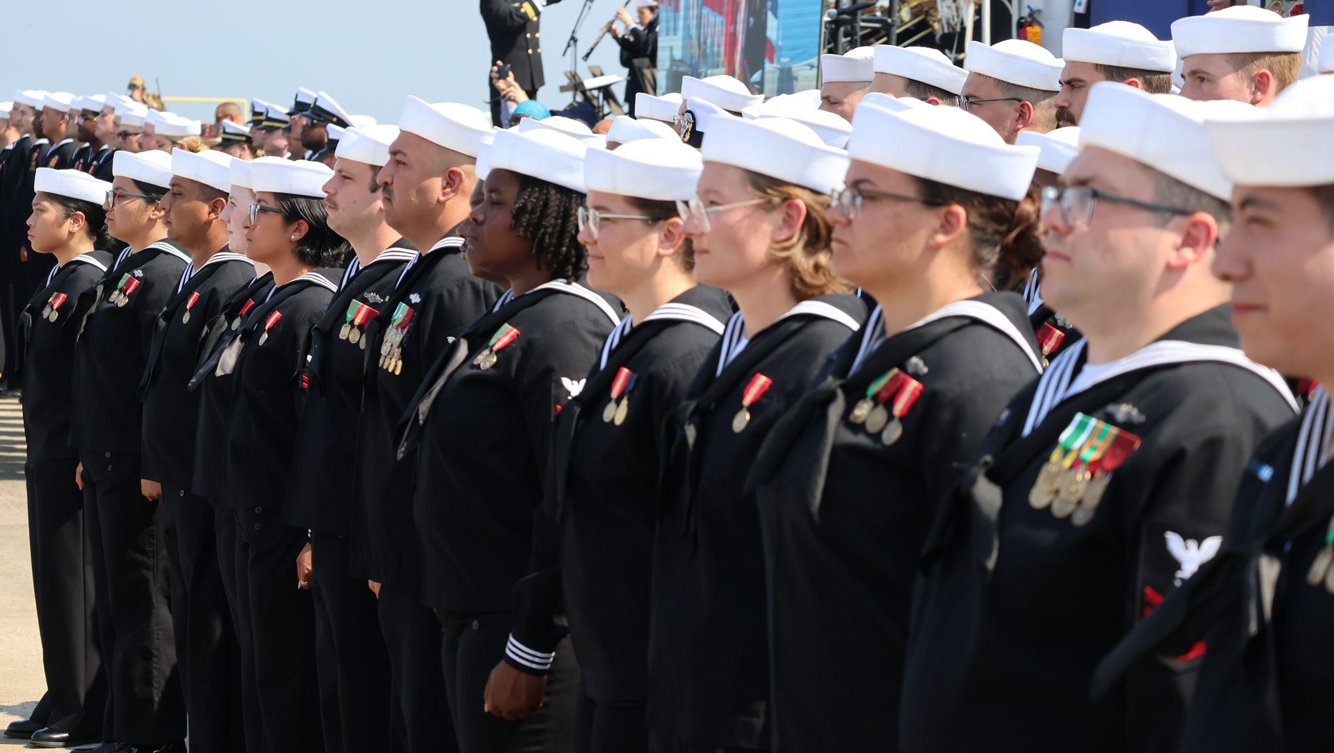 Sailors in navy uniforms stand in formation outdoors.