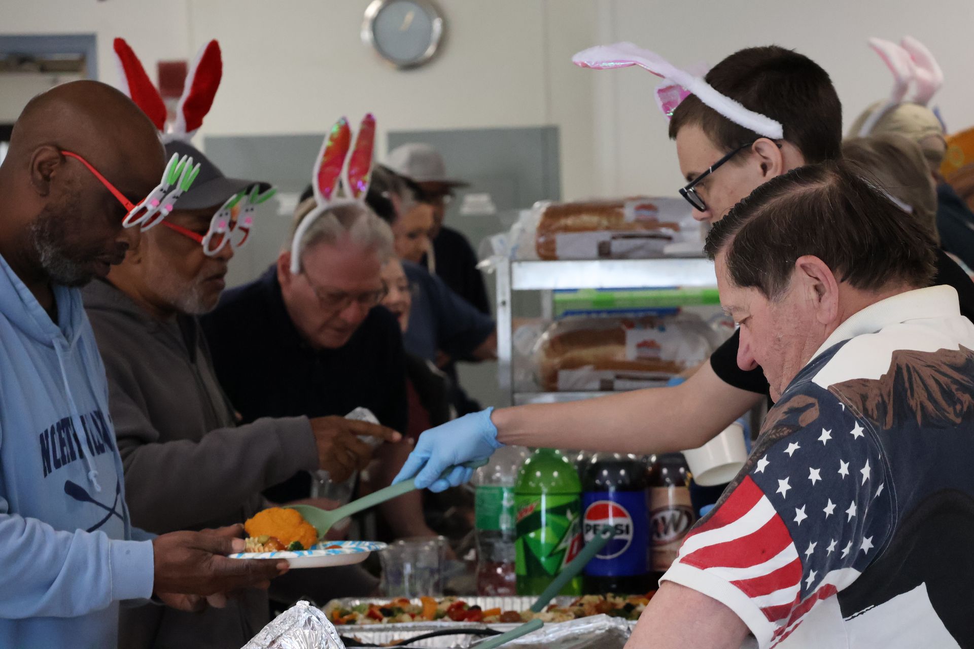 People with bunny ears serving food at a buffet. One person wears an American flag shirt.