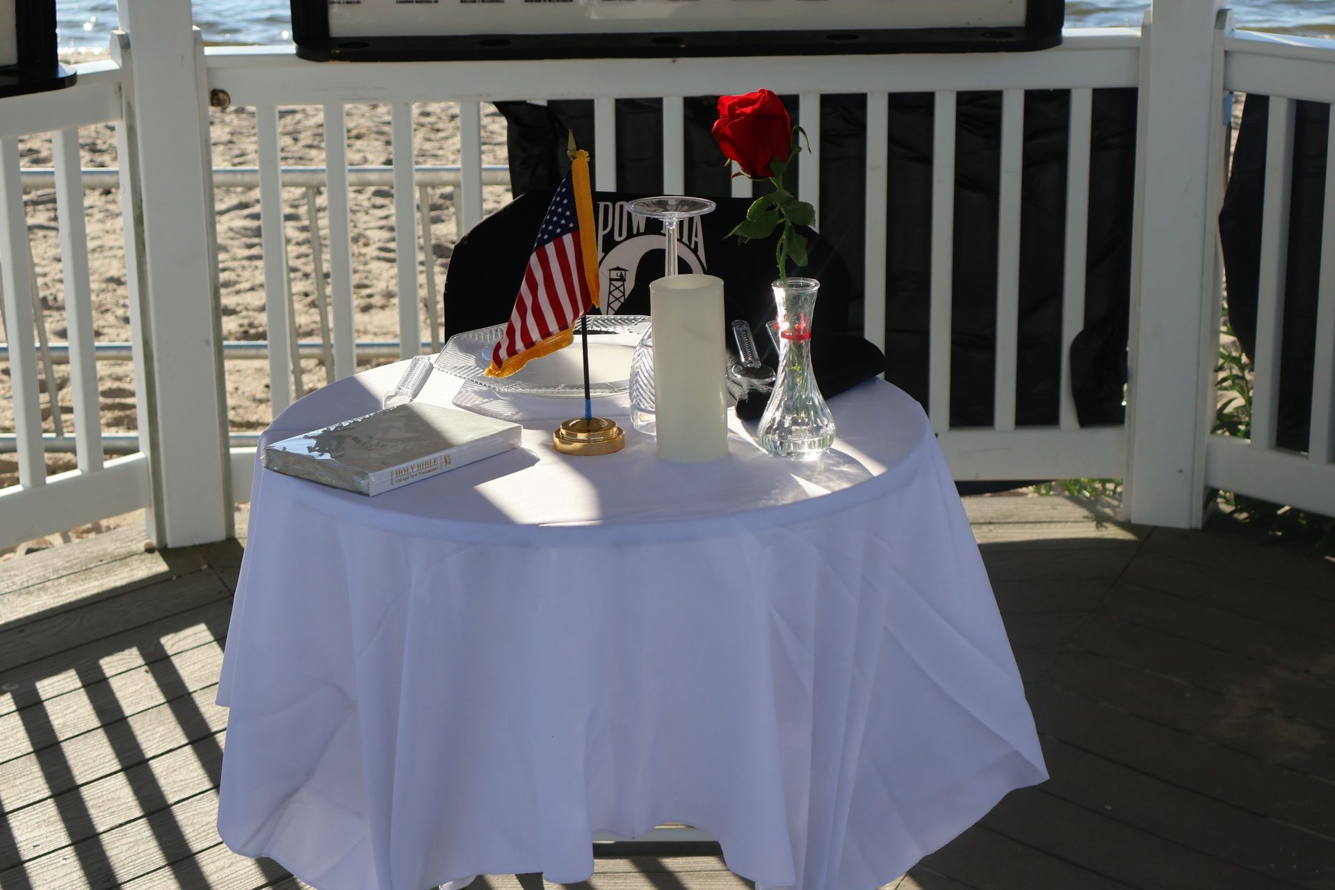 A round table draped with white cloth, set up in a gazebo. An American flag, a rose, and a candle sit on it.