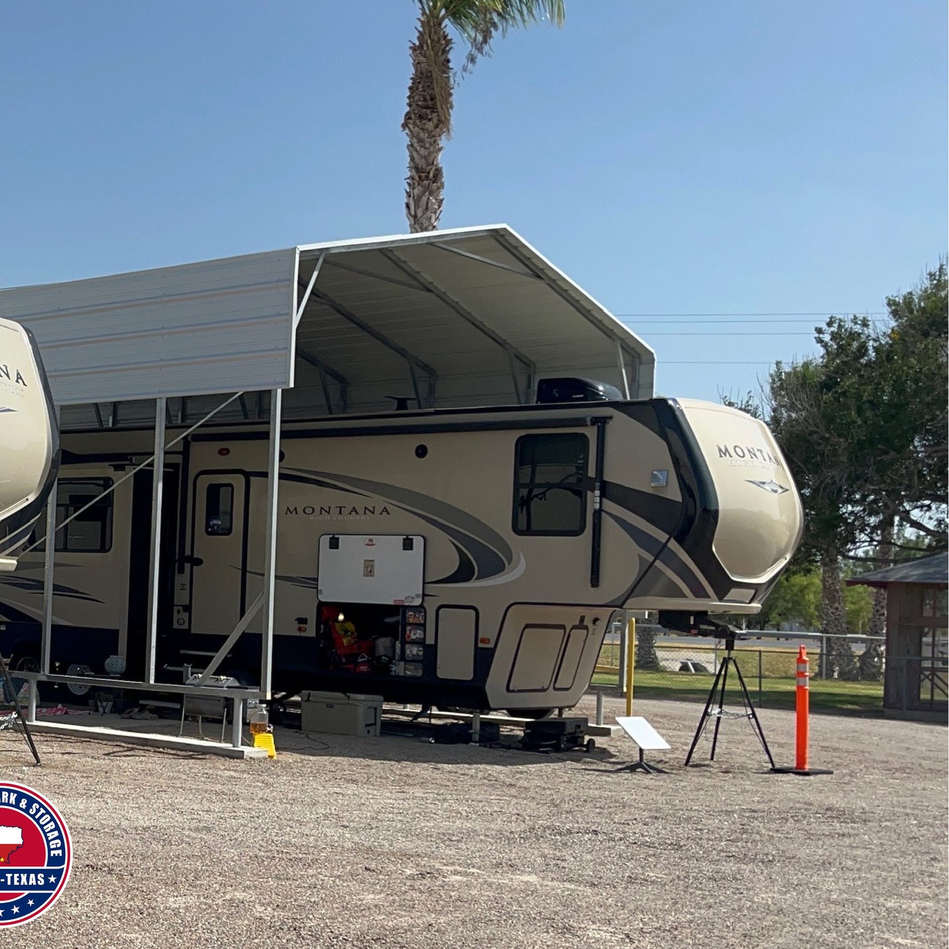 RV under a white carport on a gravel lot under a blue sky, palm tree in background.