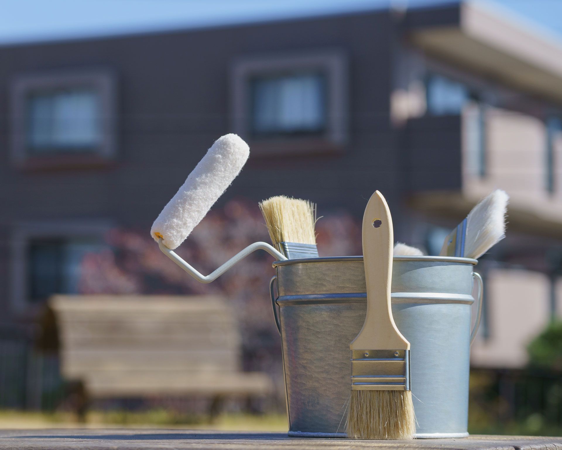 Paint supplies, paint rollers, and brushes in buckets in front of a house.