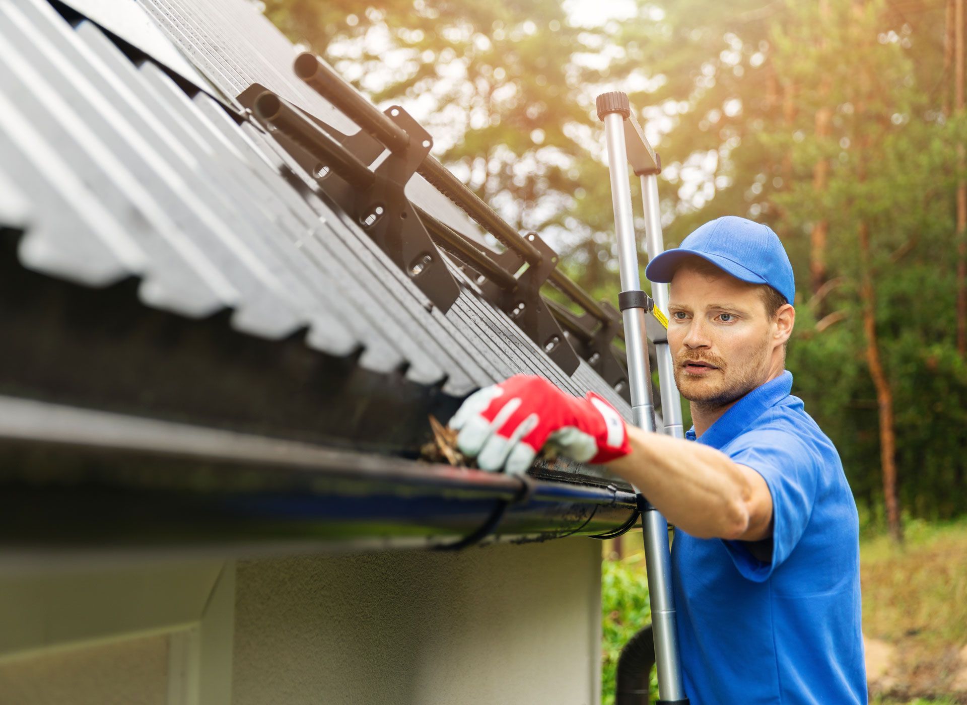 Man in blue, red gloves, cleaning roof gutters.