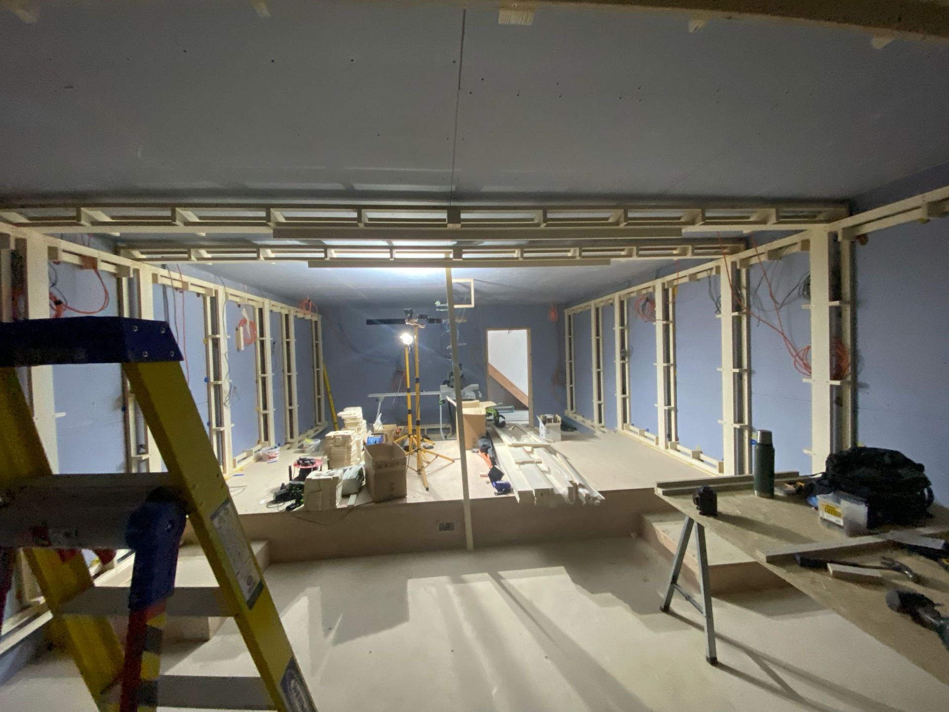 Interior room under construction, with wooden frames, blue drywall, tools, and a ladder.