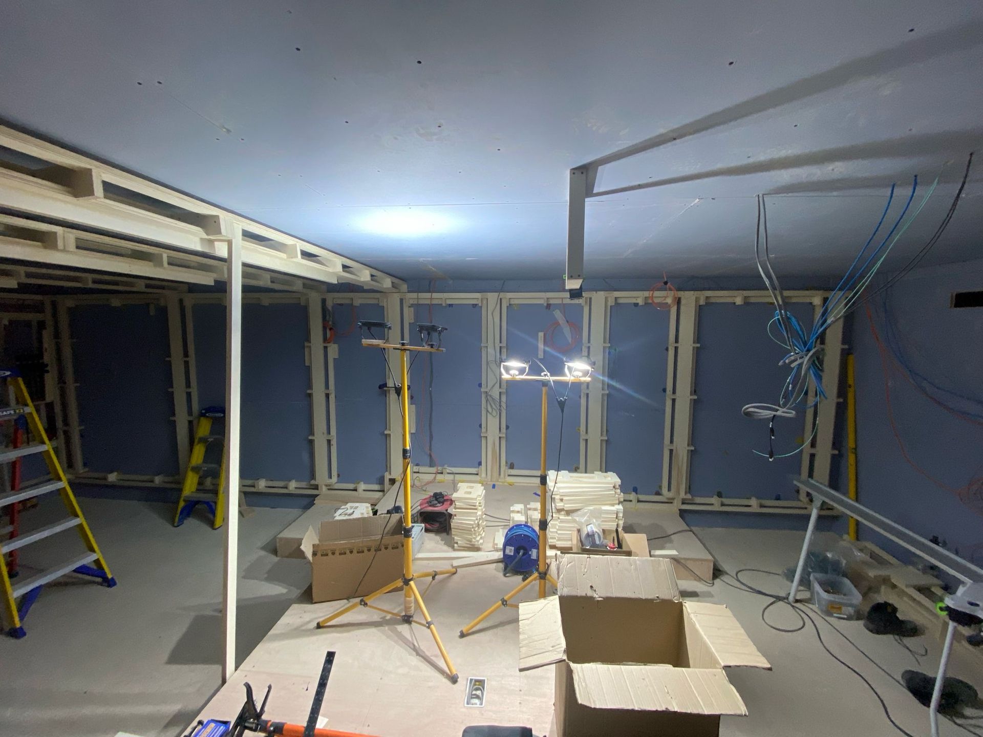 Interior of home cinema room under construction, with wooden frames, drywall, work lights, and boxes.