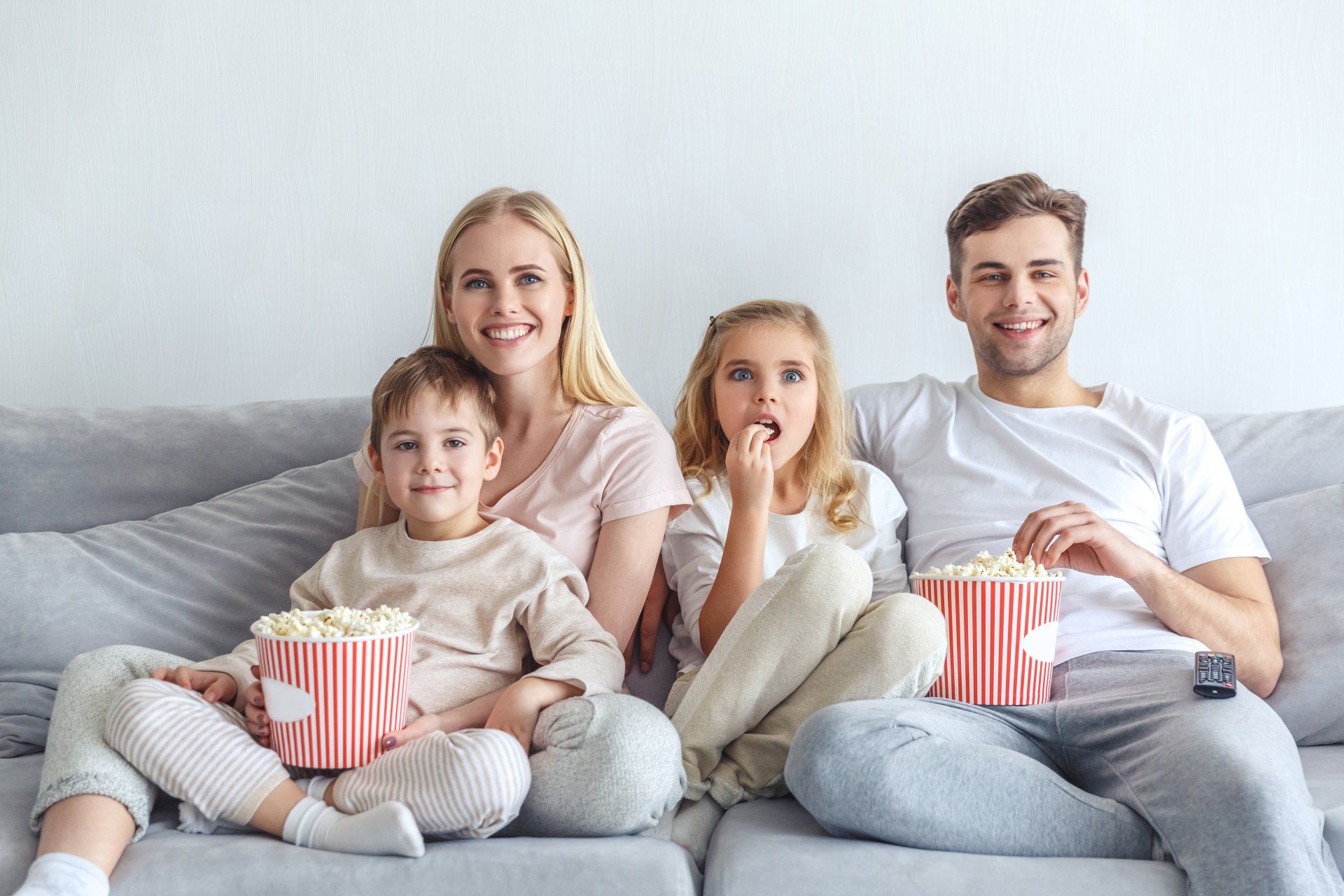 A photograph of a family, a man and woman along with a young boy and girl, sat on a sofa eating popcorn