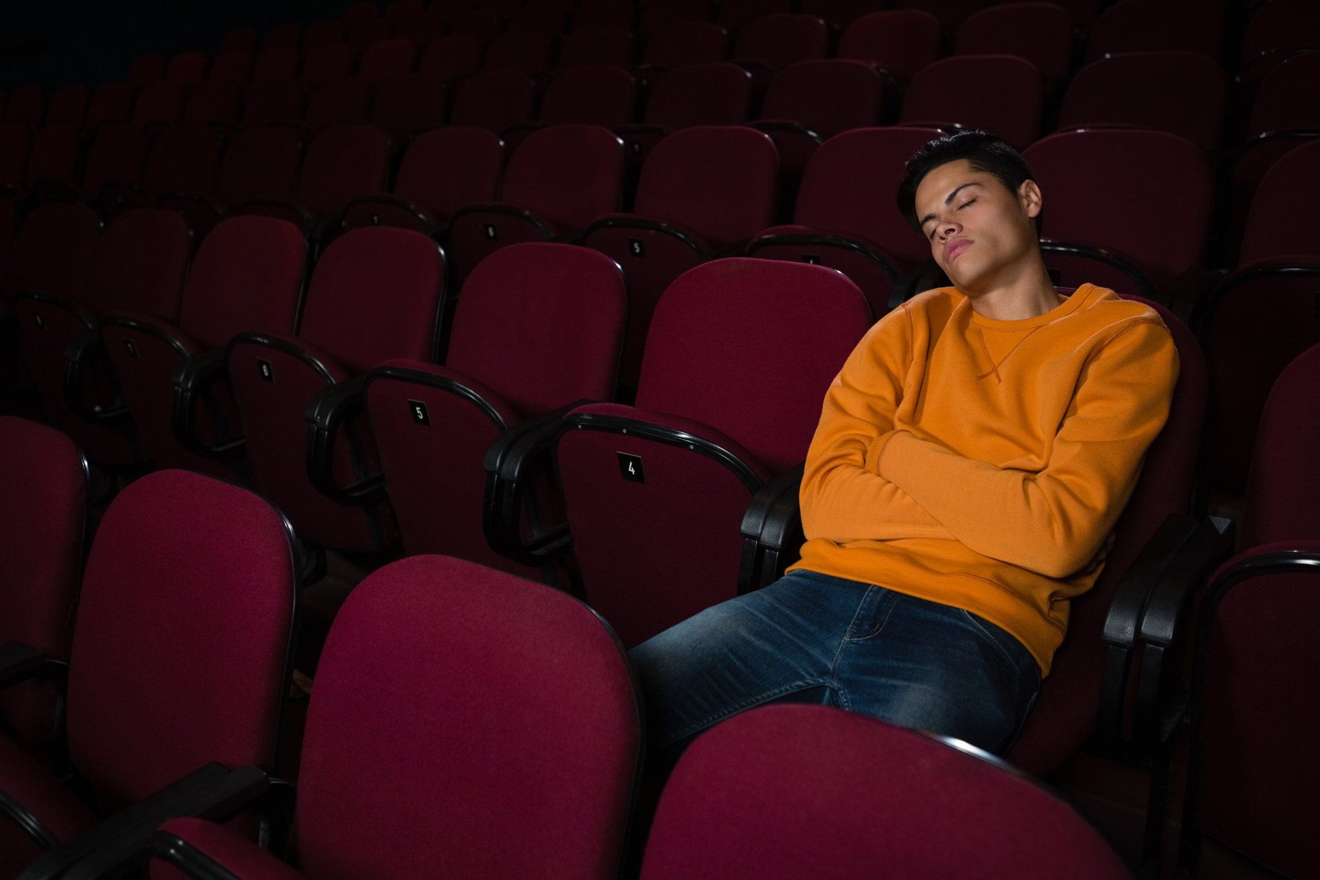 A photograph of a man, sat alone in a cinema auditorium, asleep on his seat