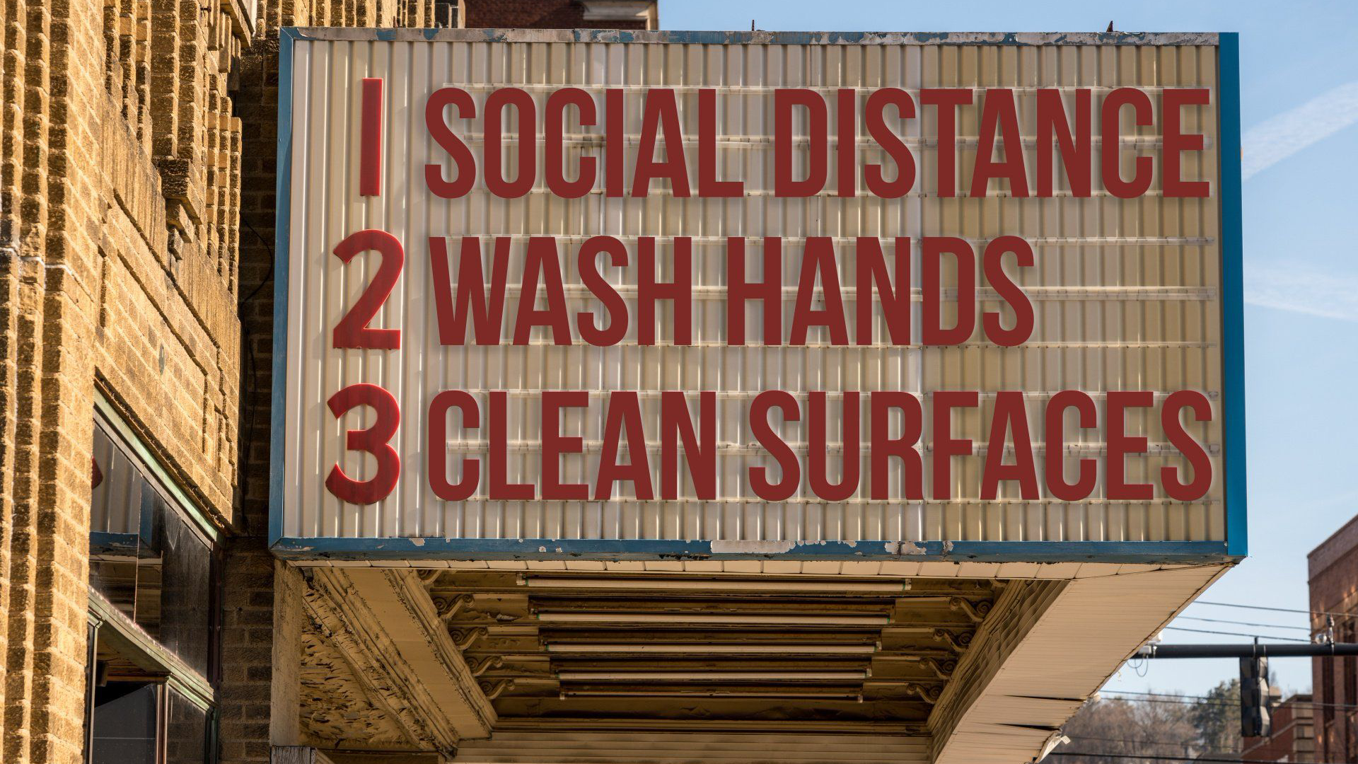 Photograph of a cinema bill board with letter stuck on to it saying 1. Social Distance, 2. Wash Hands and 3. Clean Surfaces