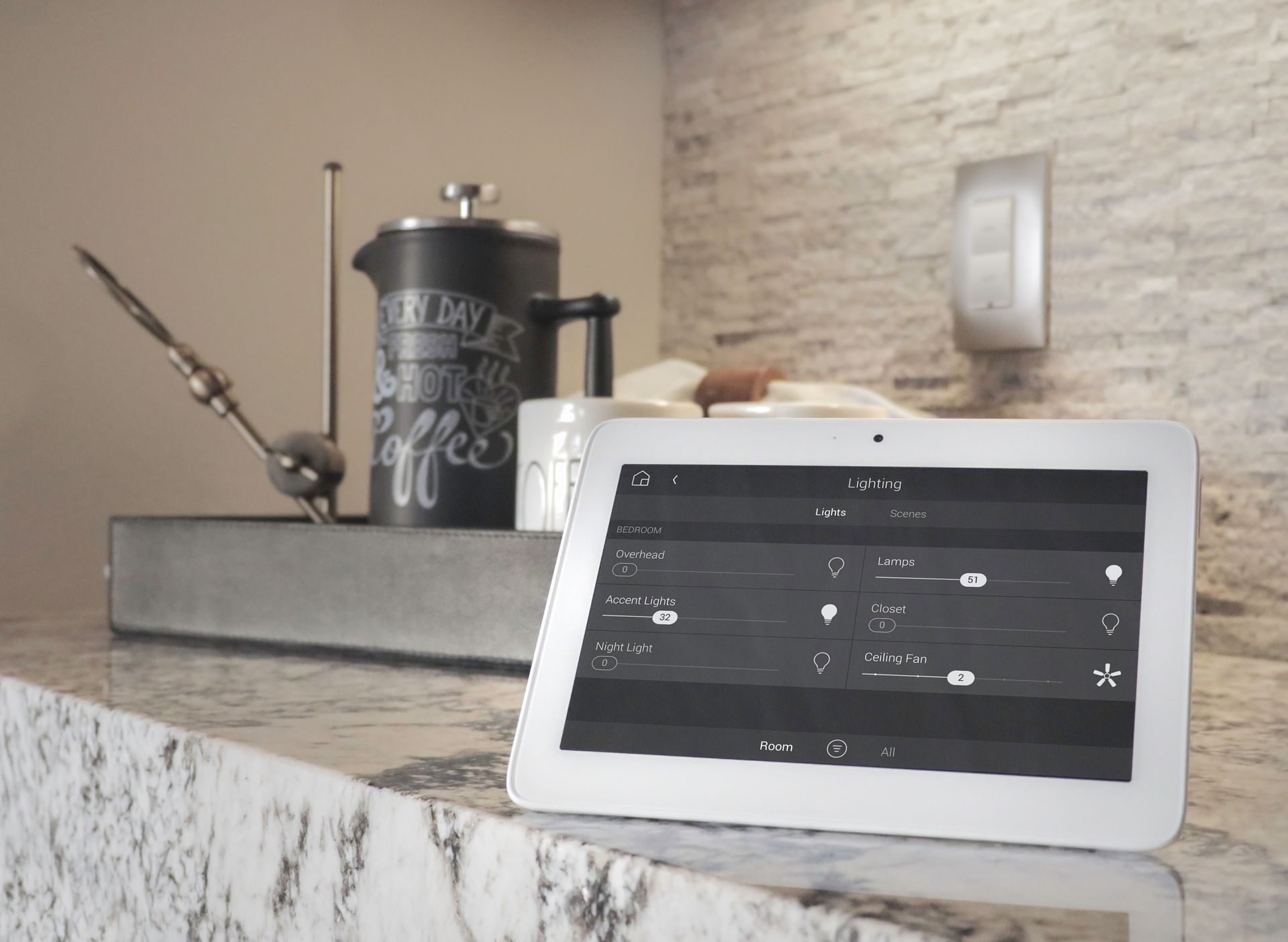 Control4 tablet on a counter with a coffee press, pen, and clock in the background.