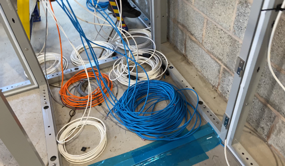Photograph of non-power cable loom coiled in cupboard floor i.e., location of the server rack