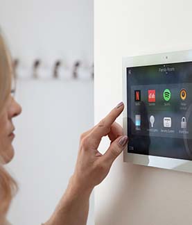 A photograph of someone's hand about to select Netflix on a Control4 Touch screen that is mounted on a wall
