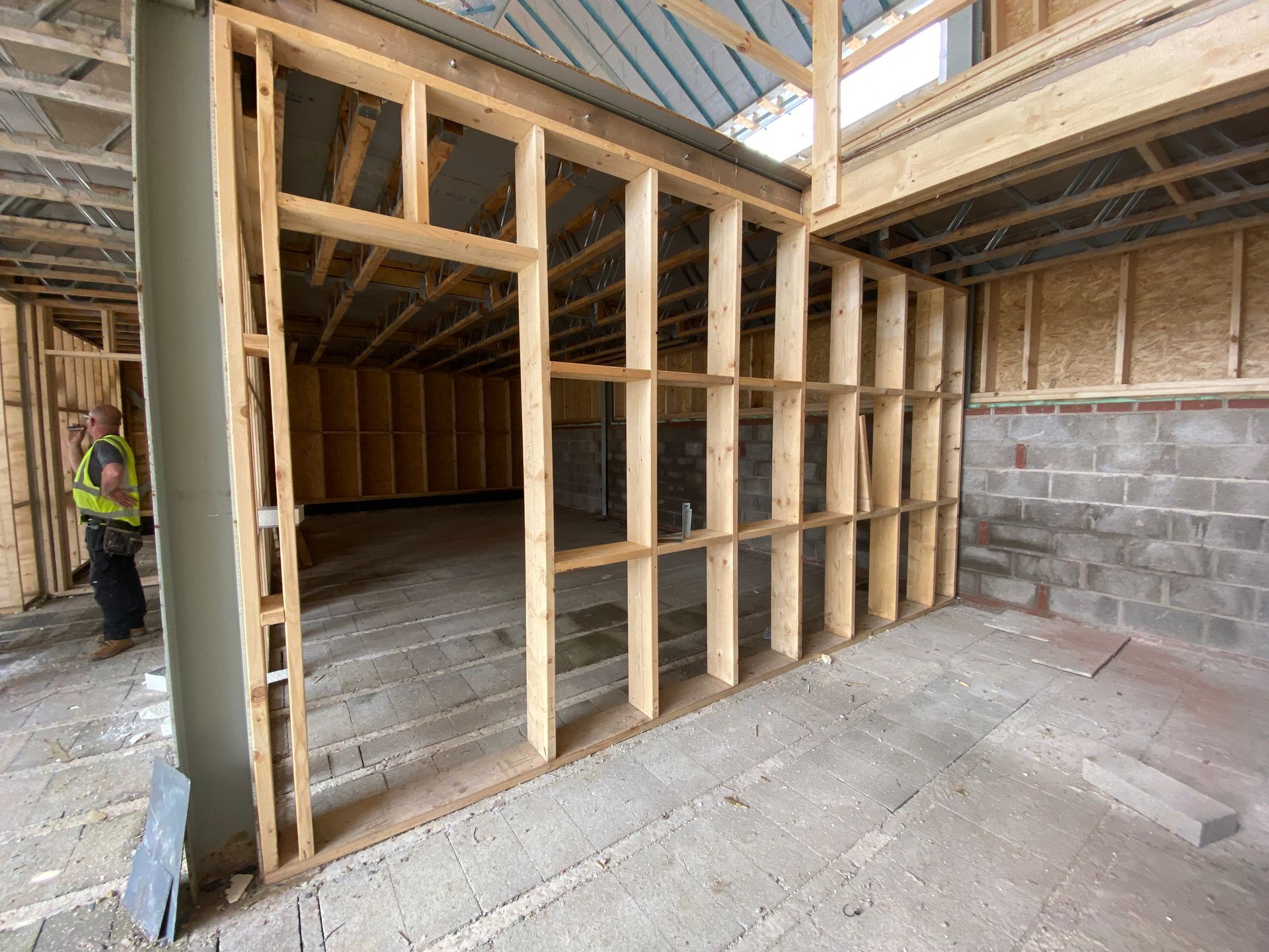 Interior construction of a building: wooden frame walls, open doorway, worker in safety vest.